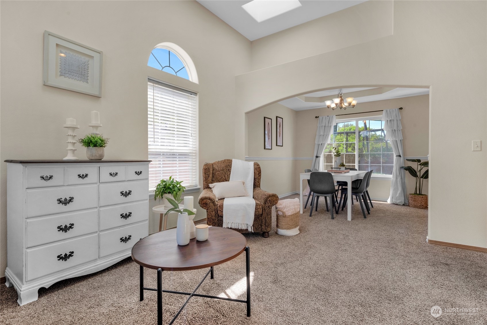 Living room with a brown armchair and round coffee table opening into a bright dining area.
