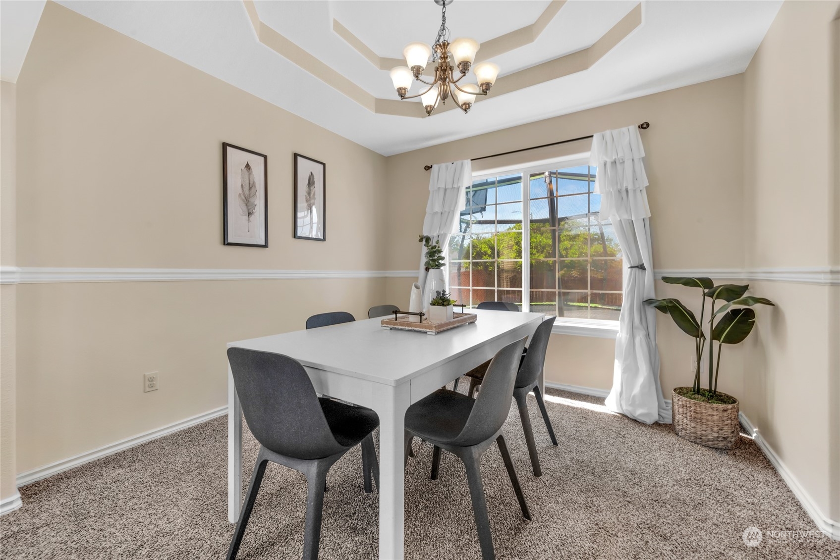Dining room with a white table, gray chairs, tray ceiling, and large curtained window.