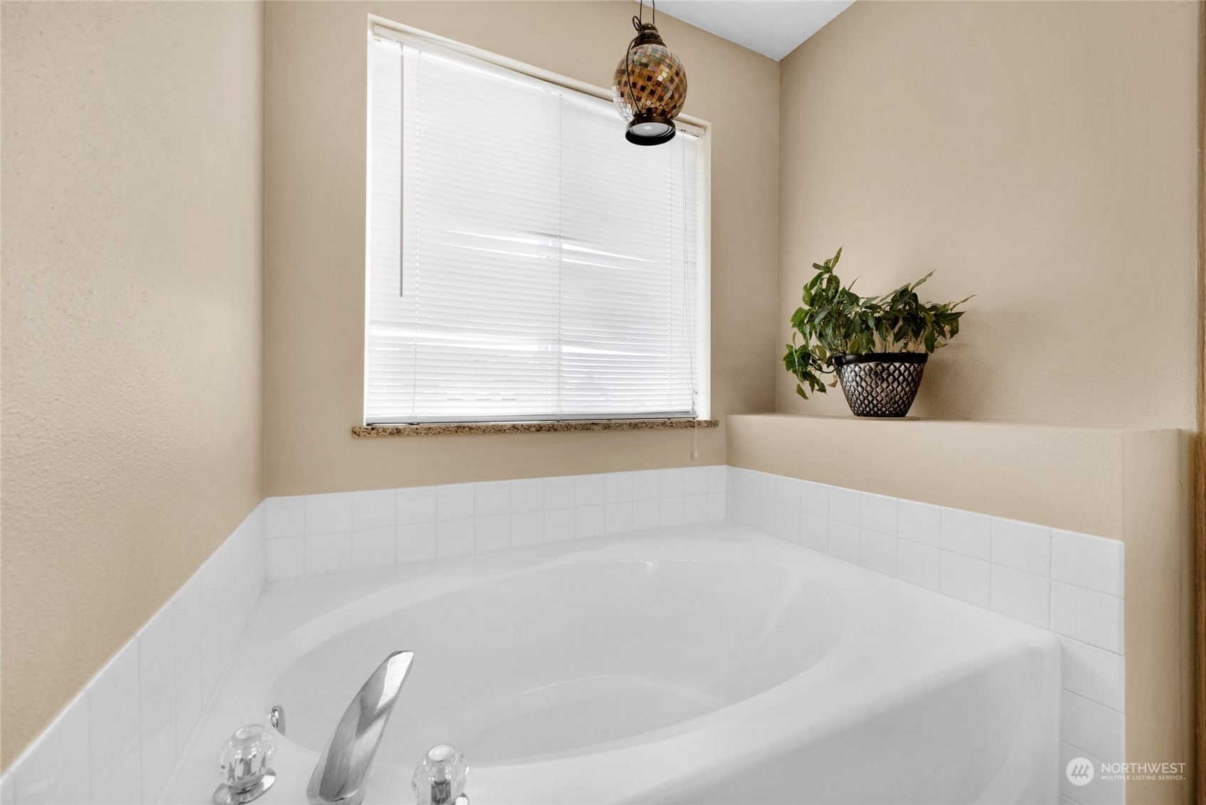 Bathroom with a large corner bathtub beneath a window and a potted plant on the ledge.