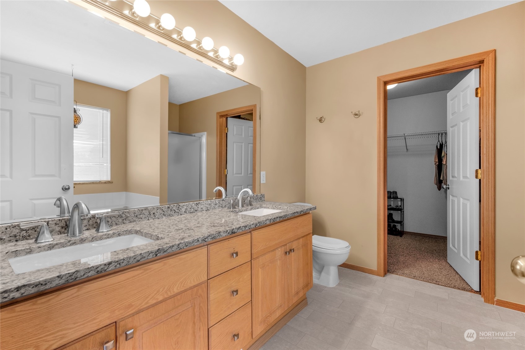 Bathroom with a double-sink granite vanity and an open doorway to a walk-in closet.