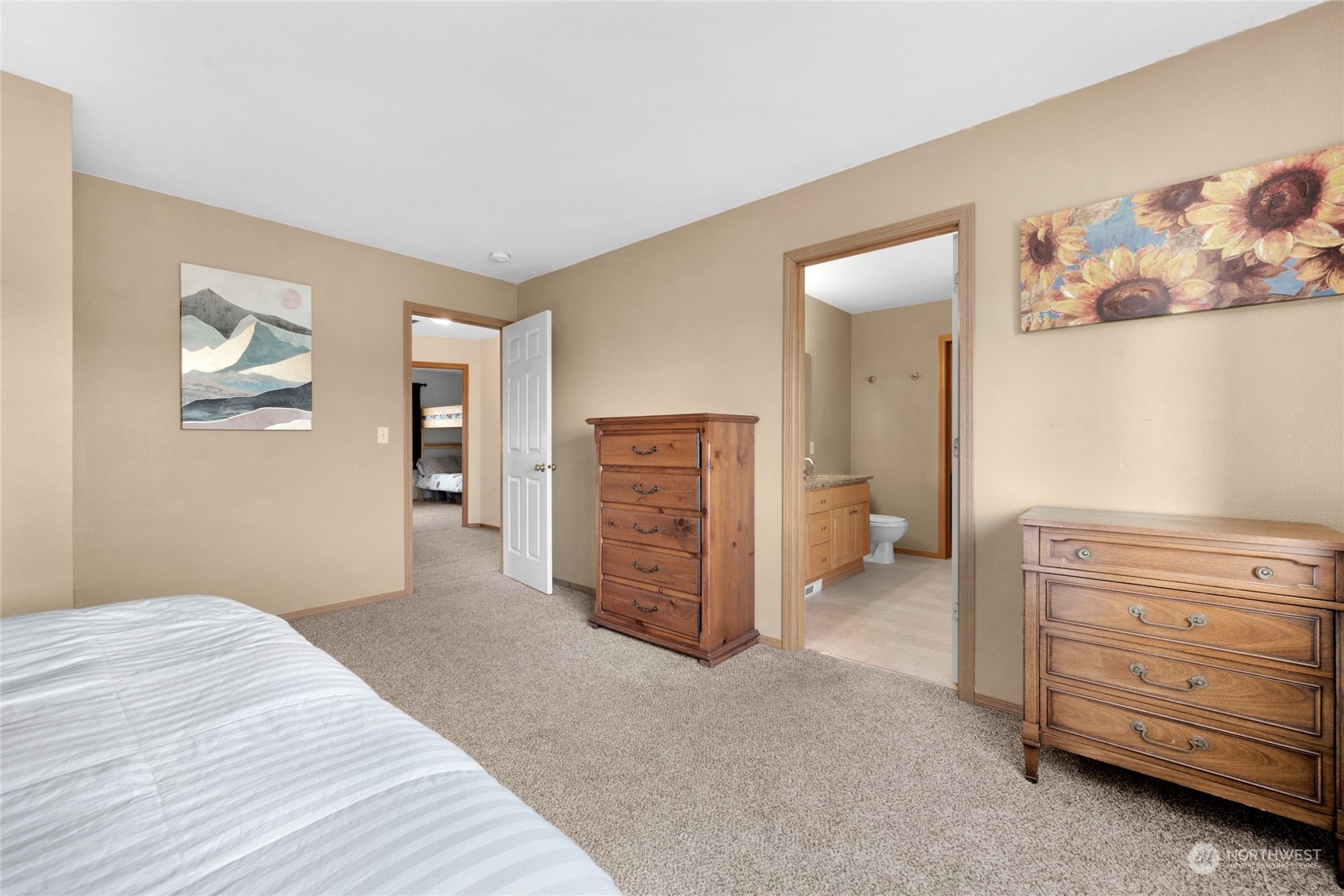 Furnished bedroom with wooden dressers, carpet, and an open doorway to an ensuite bathroom.
