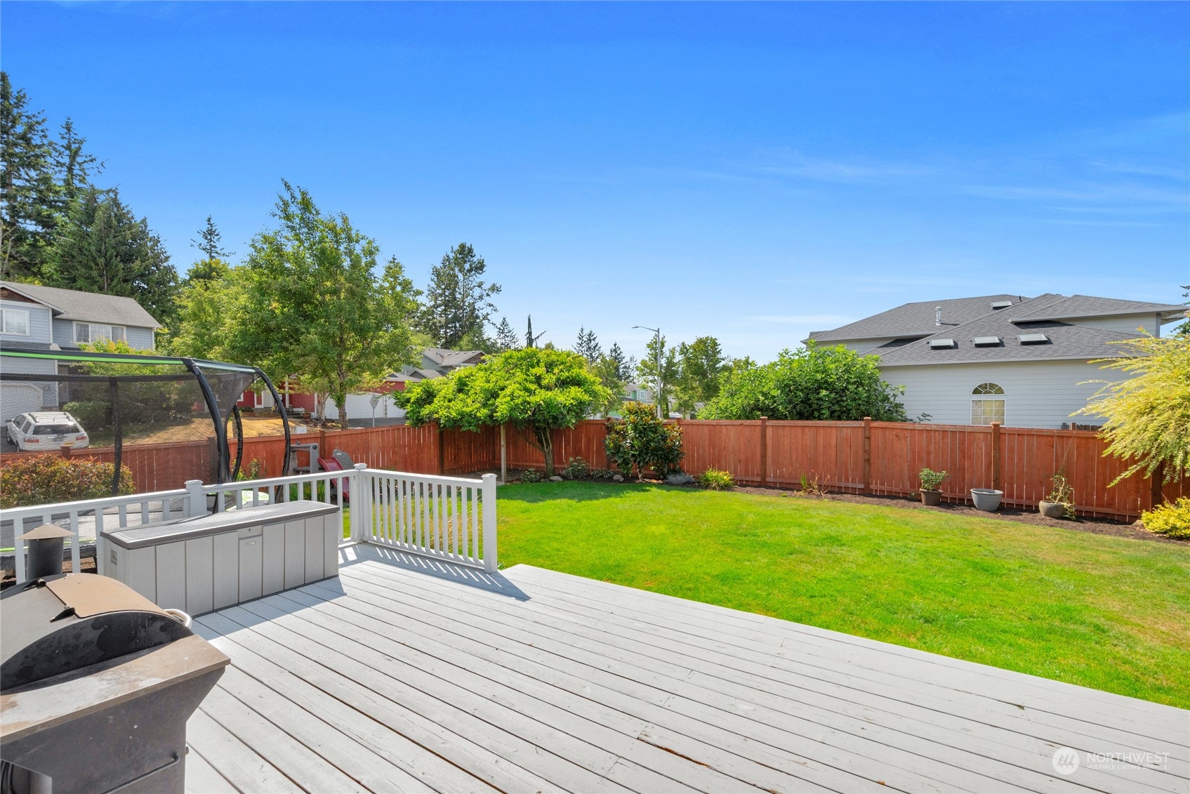 Backyard deck overlooks a fenced green lawn, with a grill and storage bench on the deck.