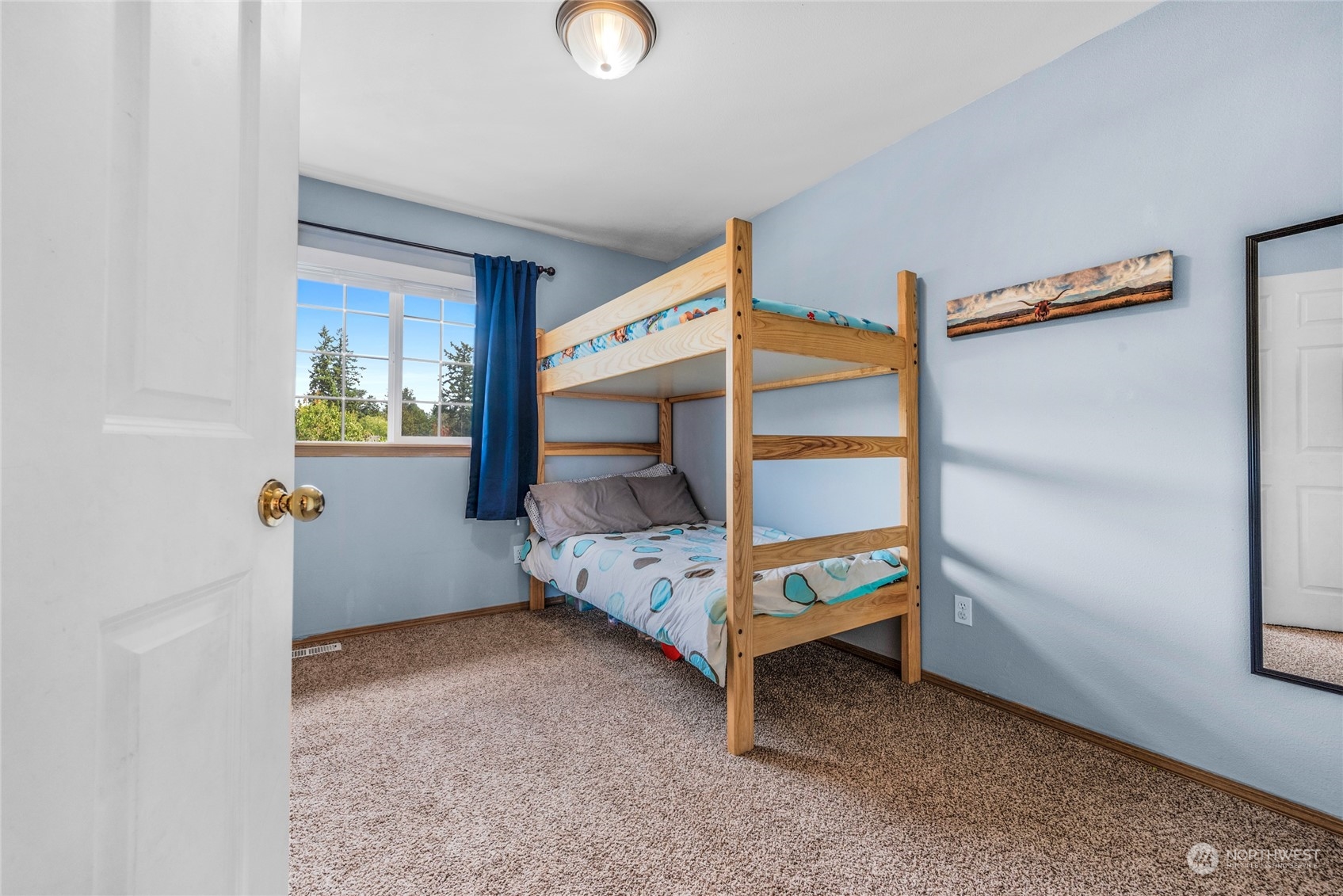 Bedroom with a wooden bunk bed, blue walls, and a window overlooking trees.