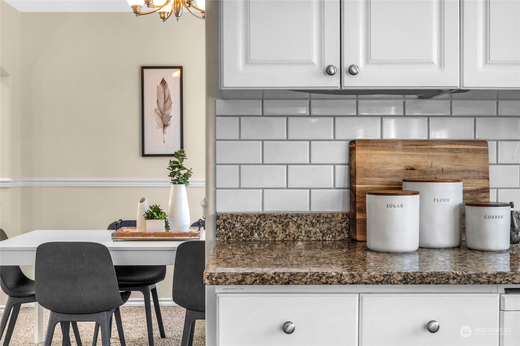 Kitchen counter with white cabinets, subway-tile backsplash, granite countertop, and labeled canisters beside the dining area.