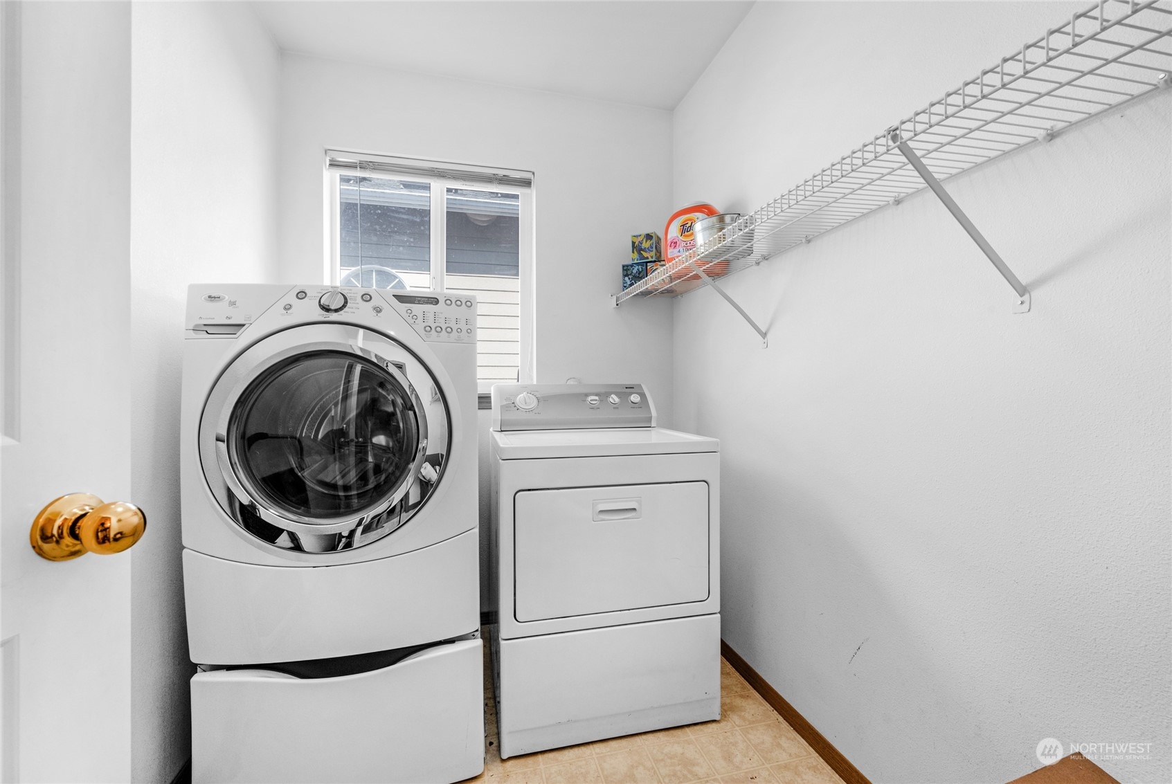 Laundry room with front-loading washer, matching dryer, and wire storage shelves.