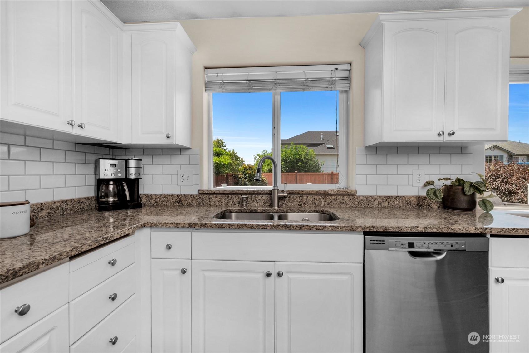 Kitchen with white cabinets, granite counters, subway-tile backsplash, and a window above the sink.