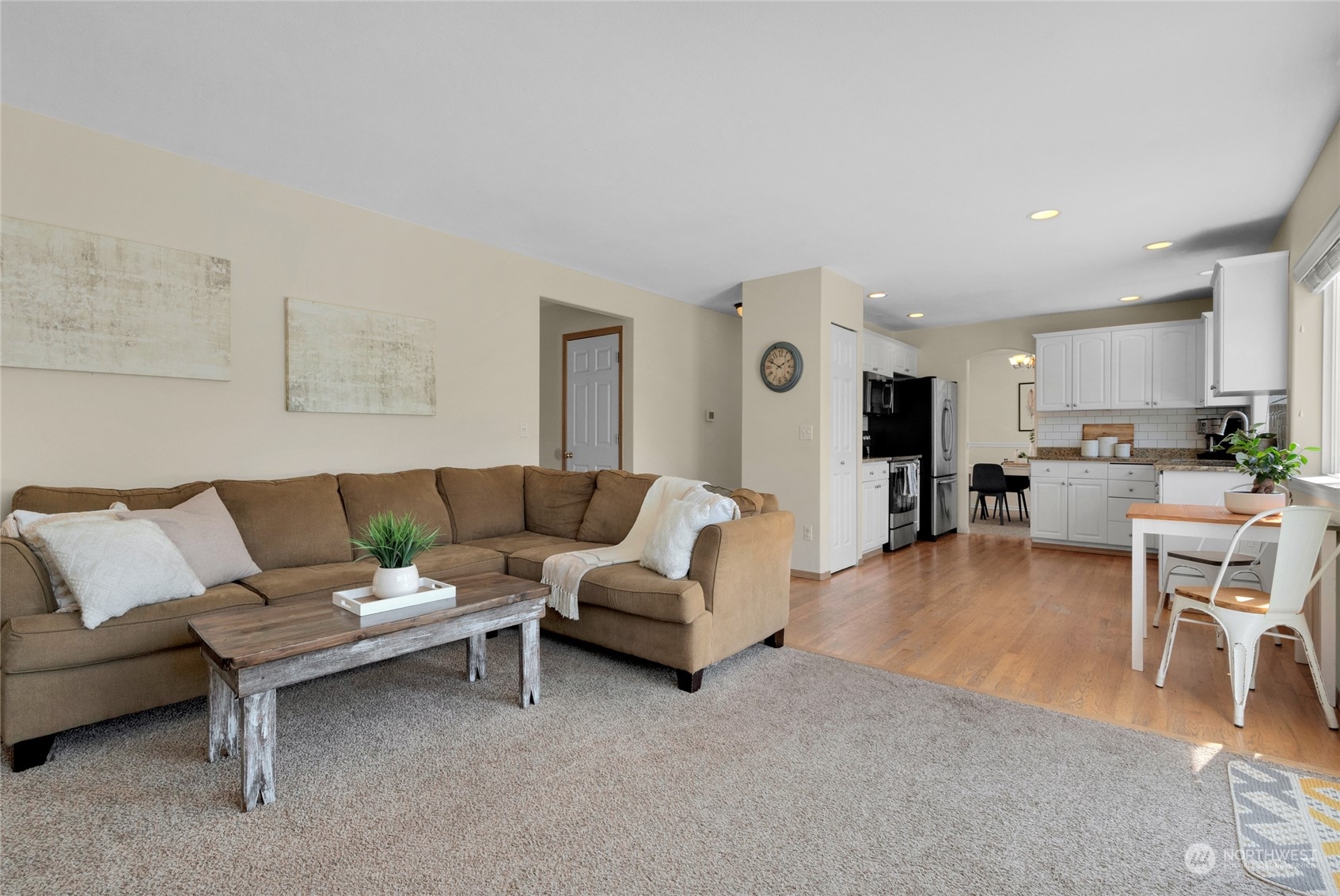 Living room with a brown sectional and rustic coffee table opening to a bright white kitchen.