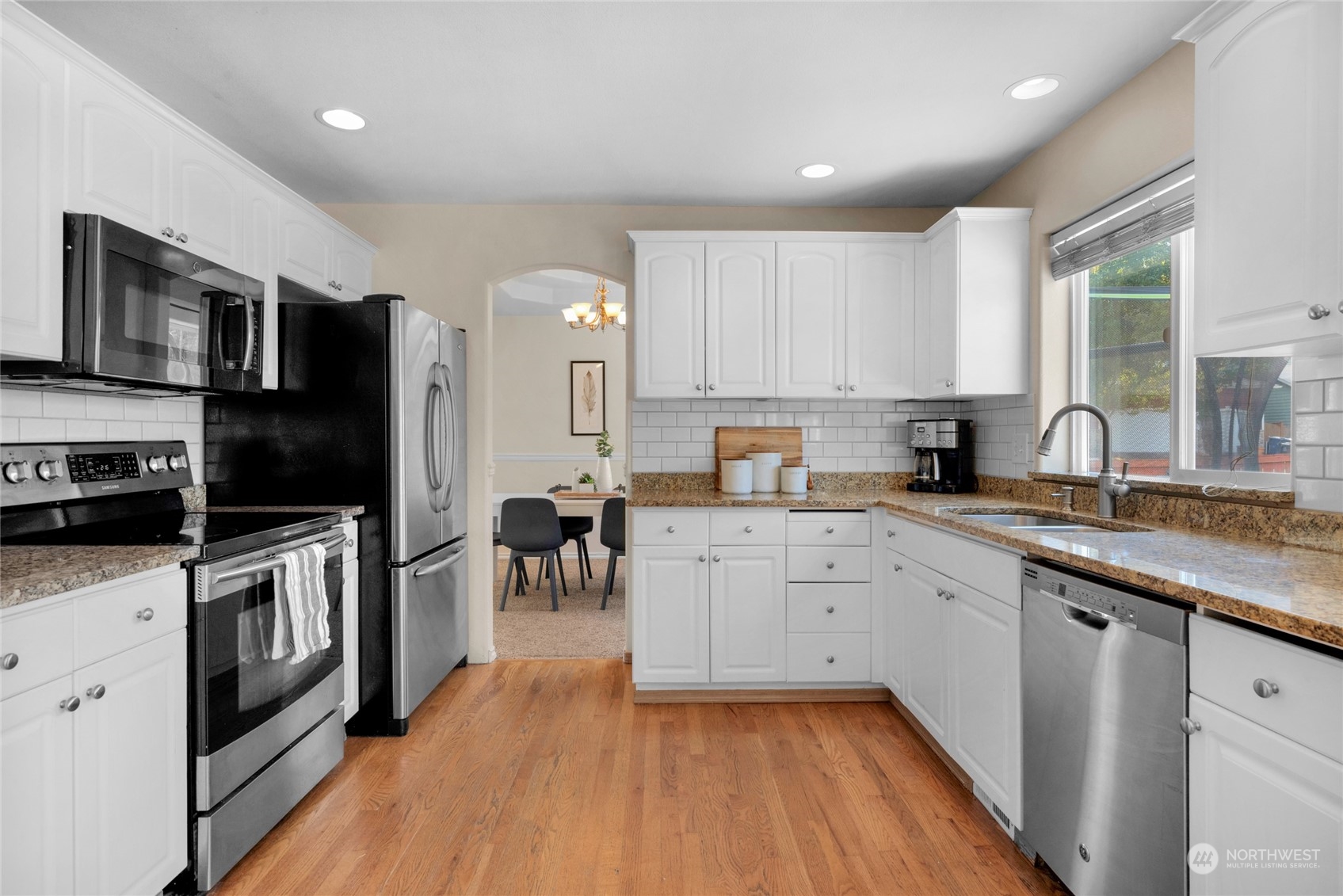 Kitchen with white cabinets, granite counters, stainless steel appliances, and hardwood floors.