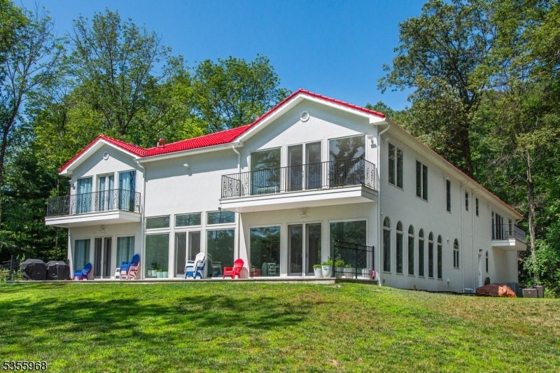 White two-story house with a red roof, two balconies, and a broad grassy lawn.
