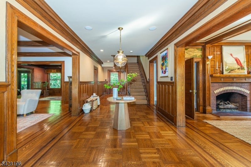 Wood-paneled entry hall with parquet floors, a staircase, and a fireplace beyond the right doorway.