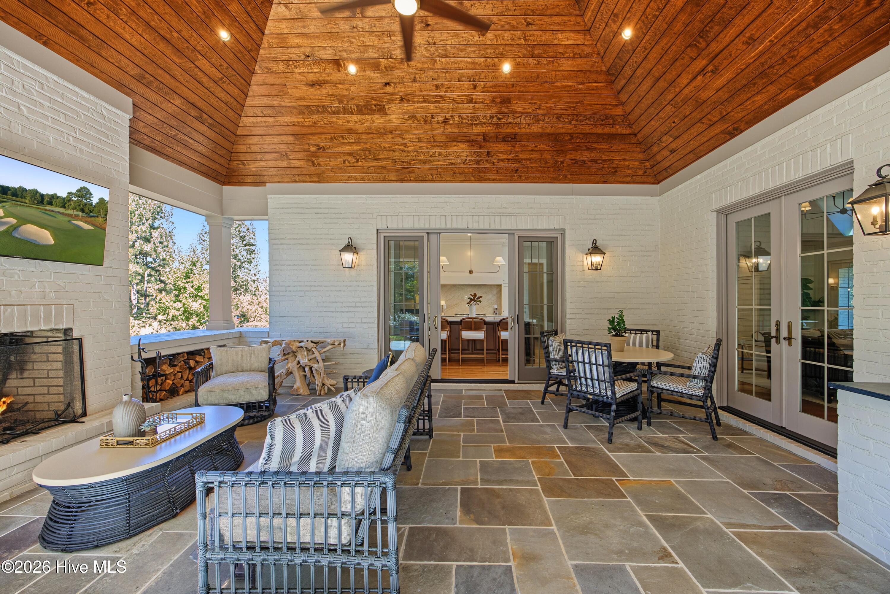 Covered patio with a vaulted wood ceiling, stone flooring, fireplace, and lounge and dining areas.