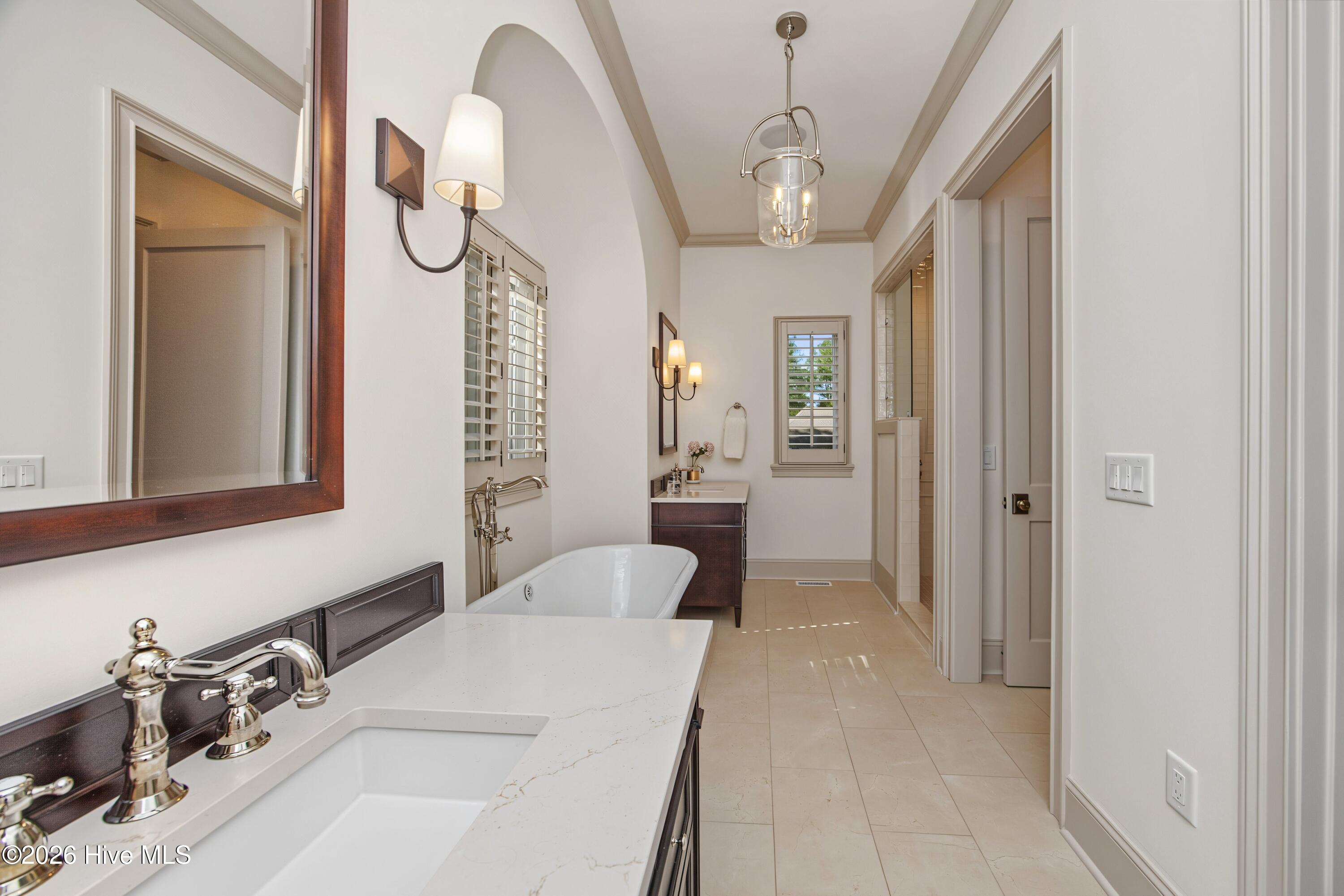 Spacious bathroom with a soaking tub beneath shuttered windows and a long white vanity.