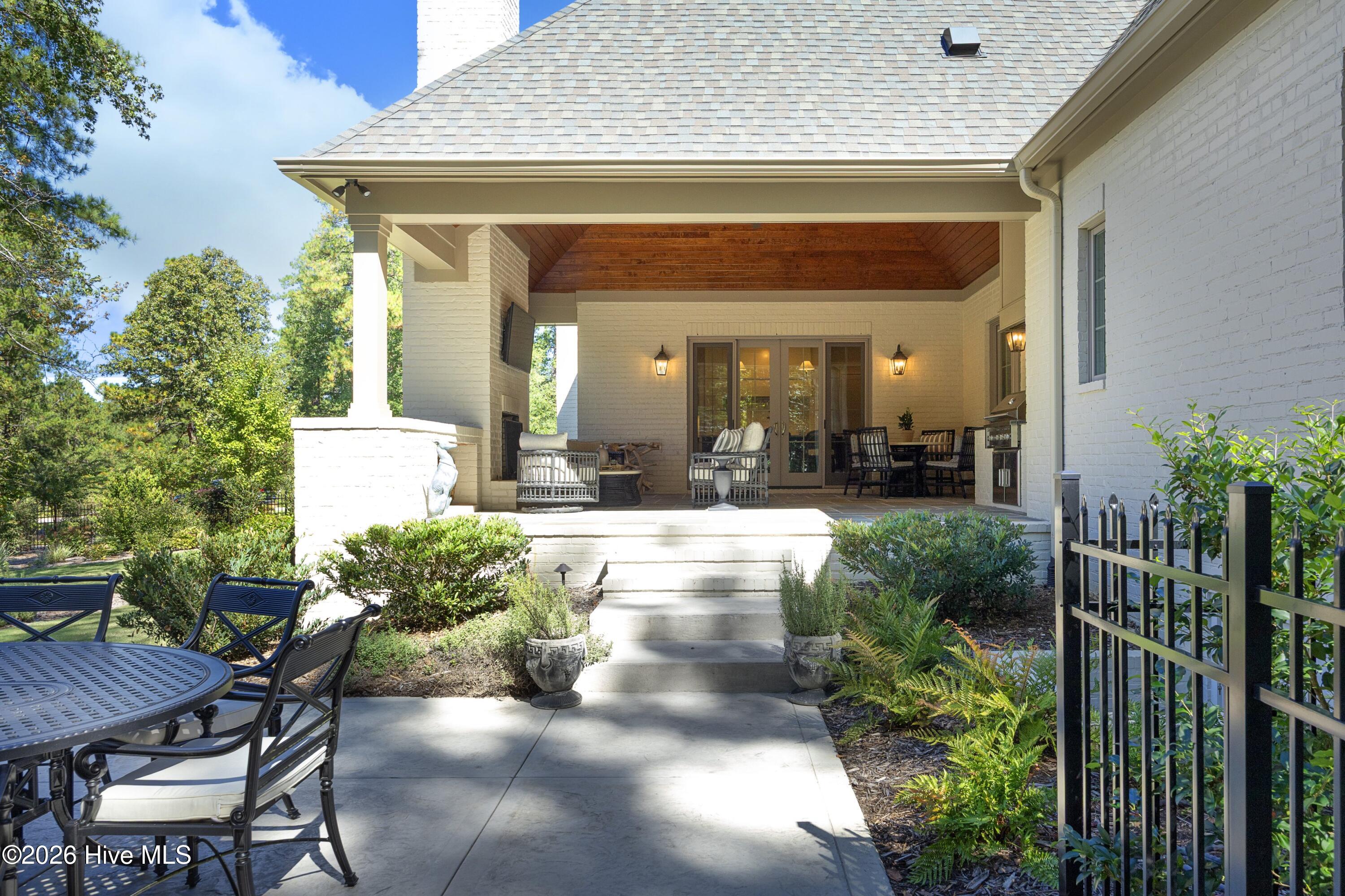 Covered patio with a wood-paneled ceiling, outdoor seating, and steps to a landscaped garden path.