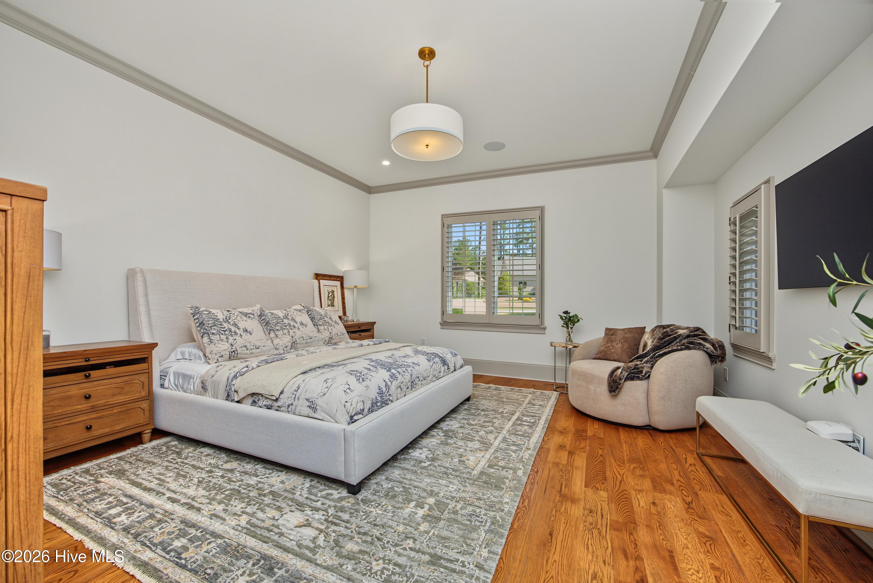 Furnished bedroom with a large upholstered bed, patterned rug, hardwood floors, and a rounded reading chair.