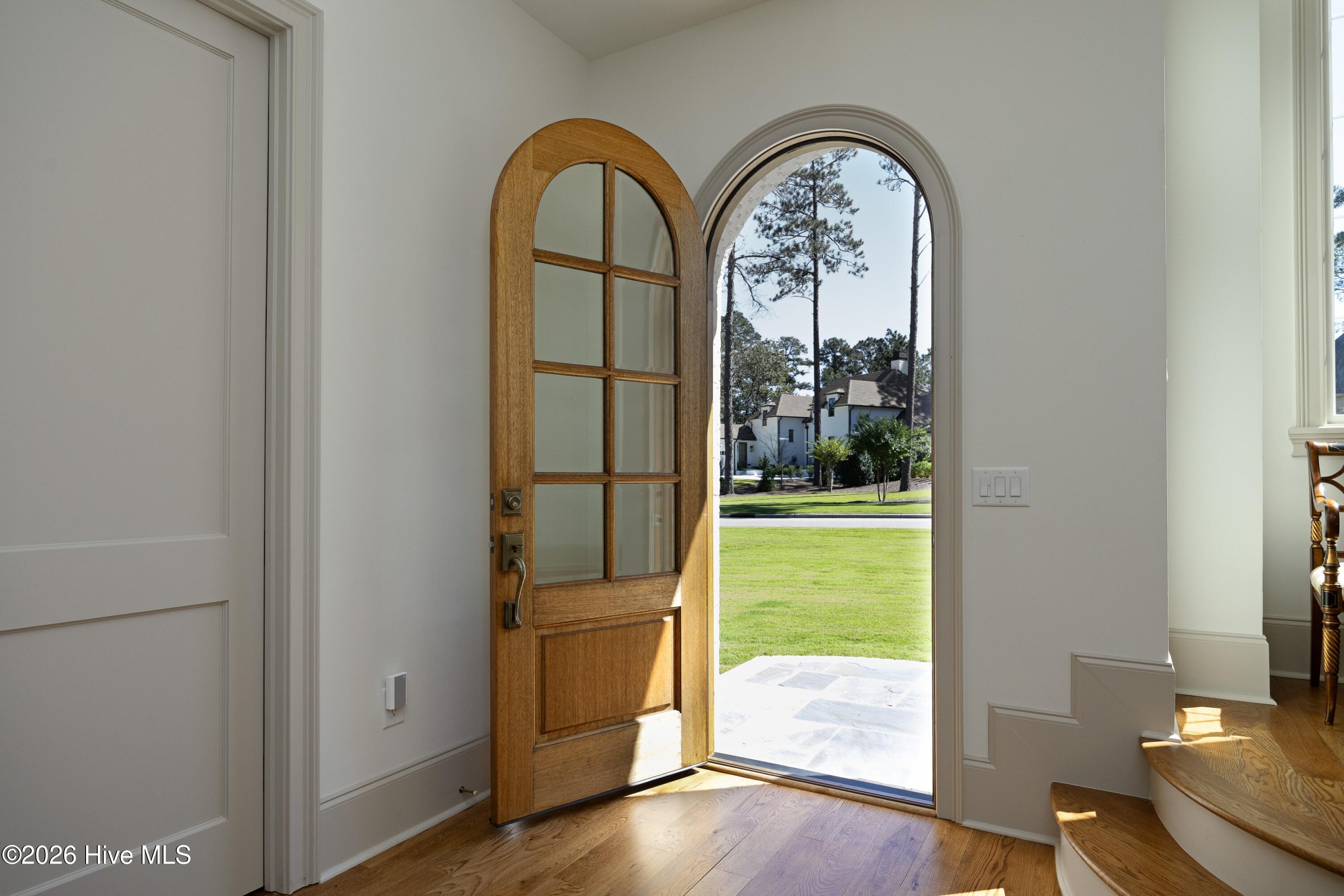 Entryway with an open arched wooden front door, hardwood floor, and curved staircase.