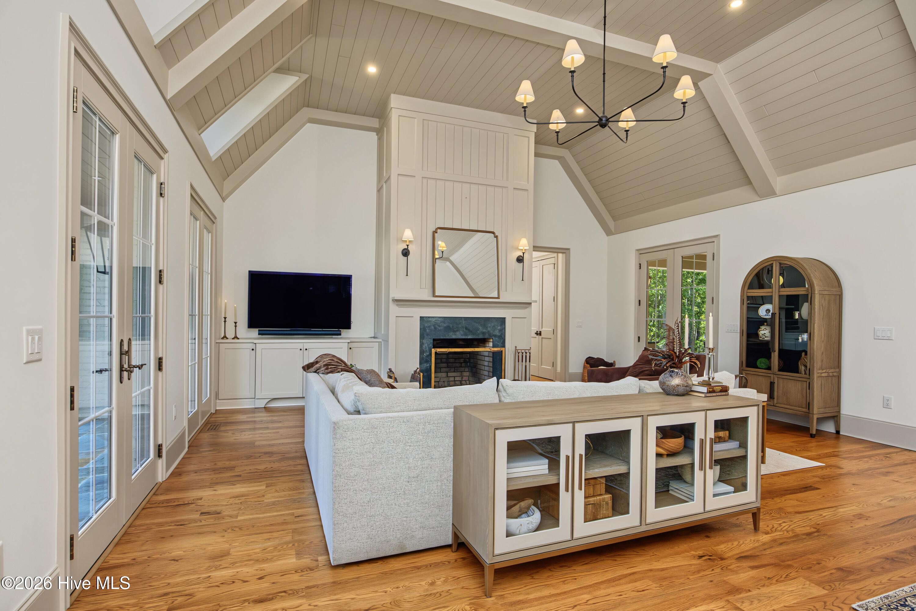 Vaulted living room with a fireplace, white sectional, hardwood floors, and French doors.