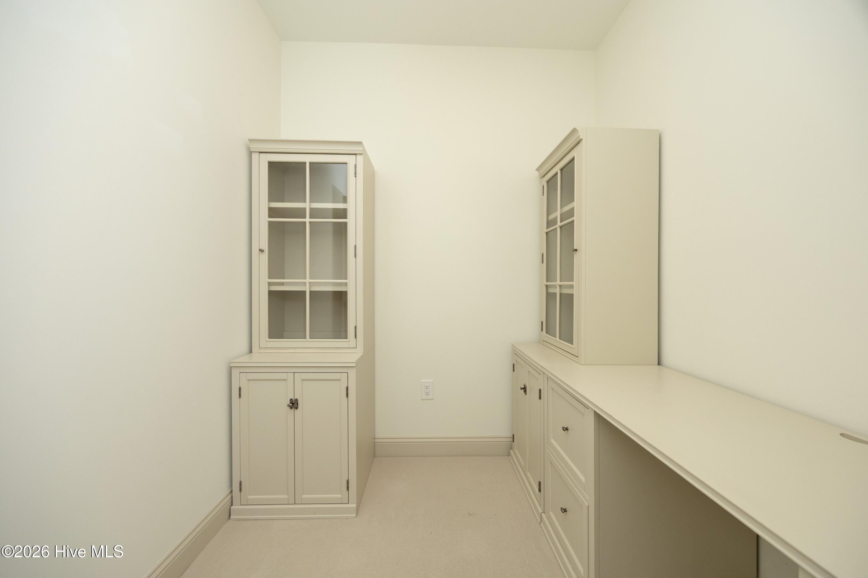 Narrow room with cream built-in glass-front cabinets and a long countertop.