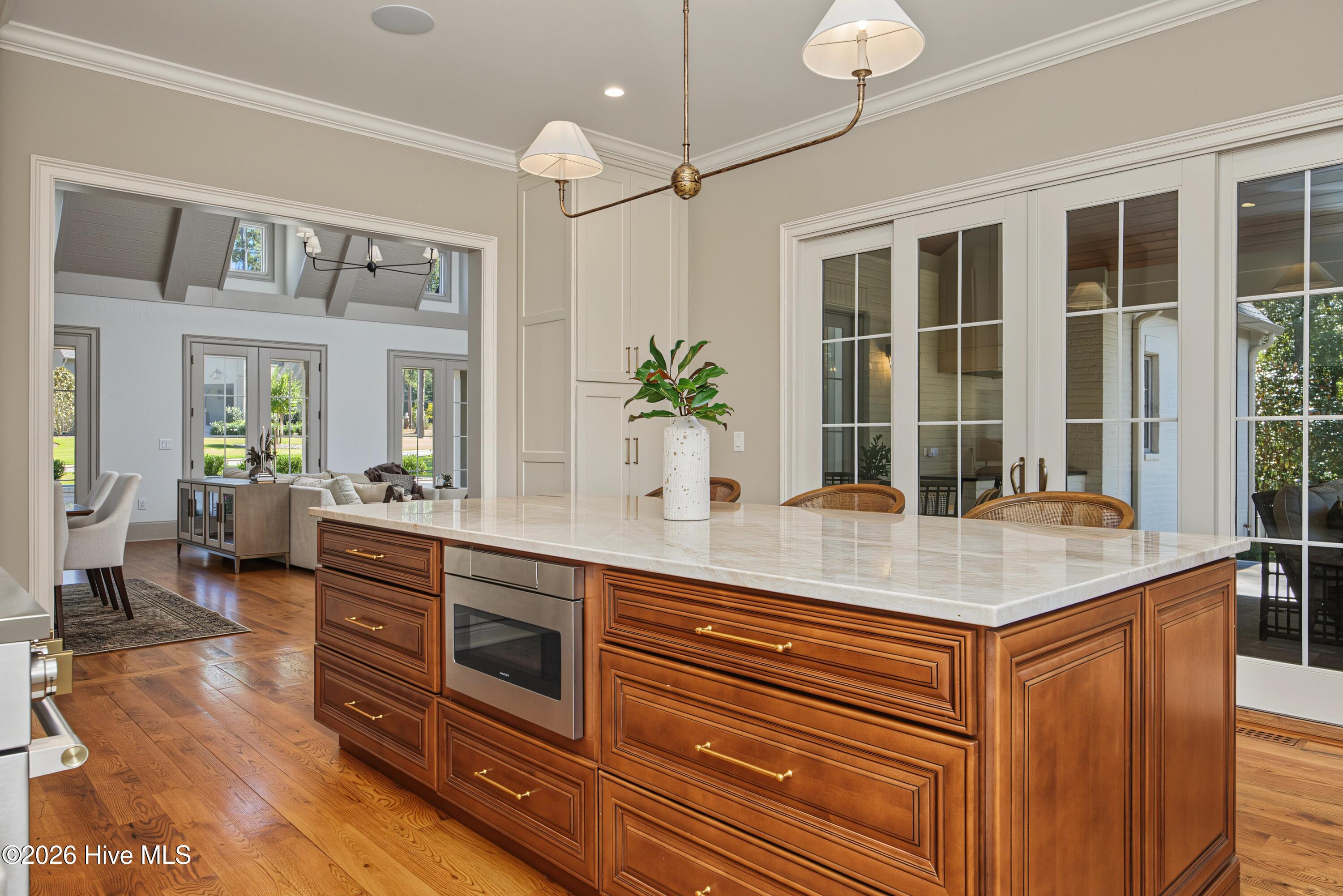 Kitchen with a large white stone island and walnut cabinetry opening to a furnished living area.