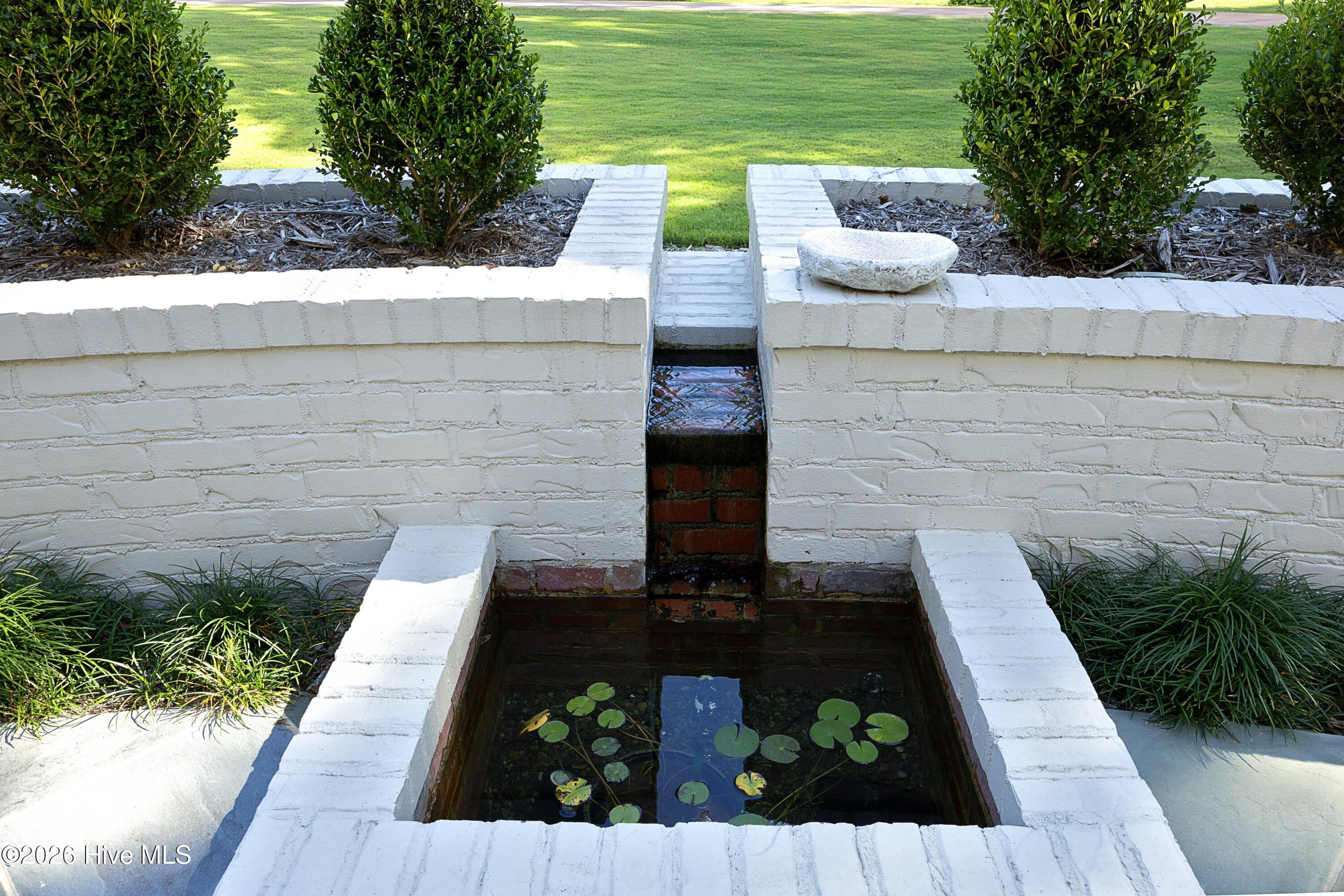 Brick-lined garden pond with lily pads and a small spillway in a white brick wall.