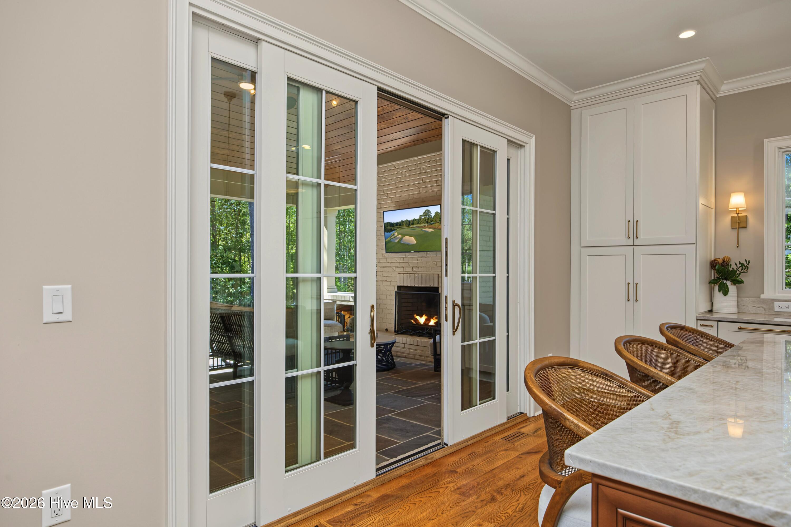 Kitchen island with woven chairs and open sliding doors to a covered patio with a fireplace.