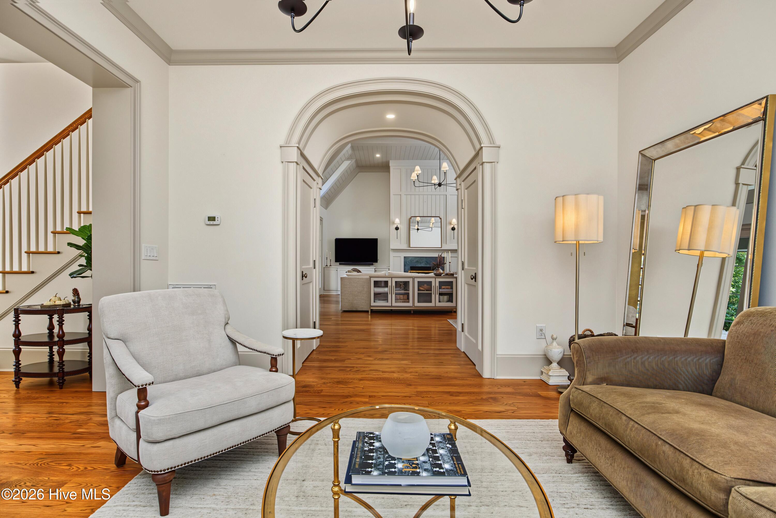 Furnished living room with a large arched opening, hardwood floors, and staircase at left.