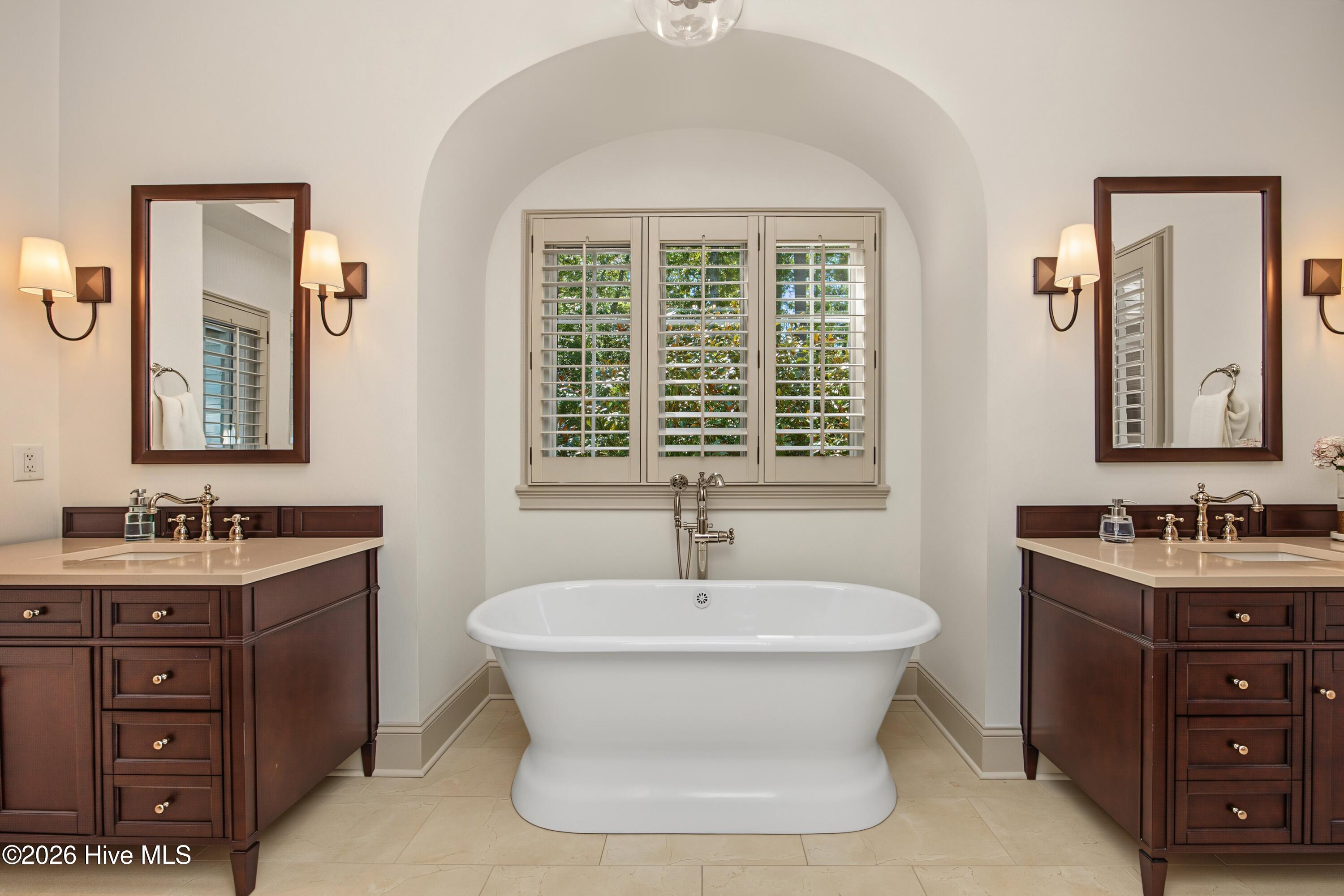 Bathroom with a freestanding soaking tub, shuttered window, and matching dark wood vanities.