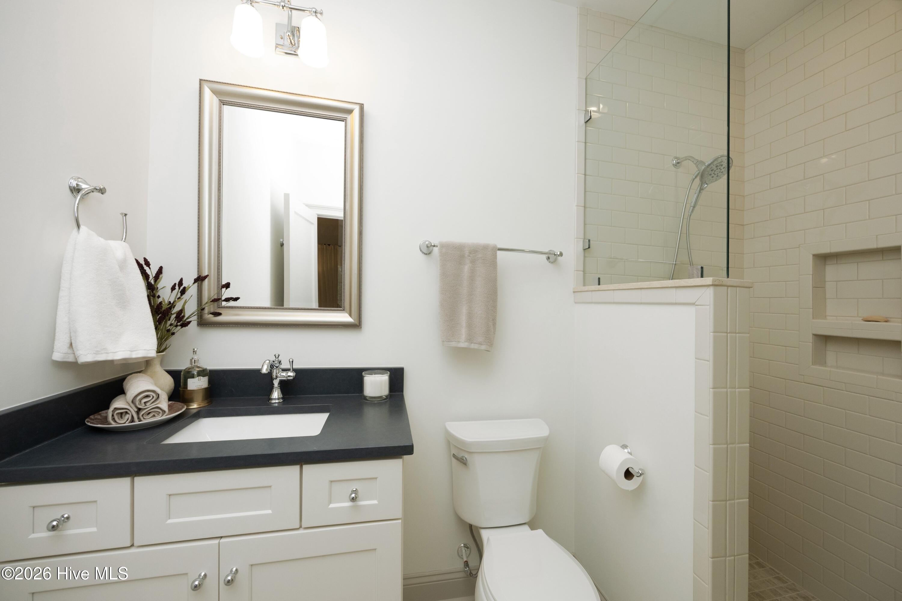 Bathroom with a dark vanity countertop, framed mirror, and glass-enclosed tiled shower.