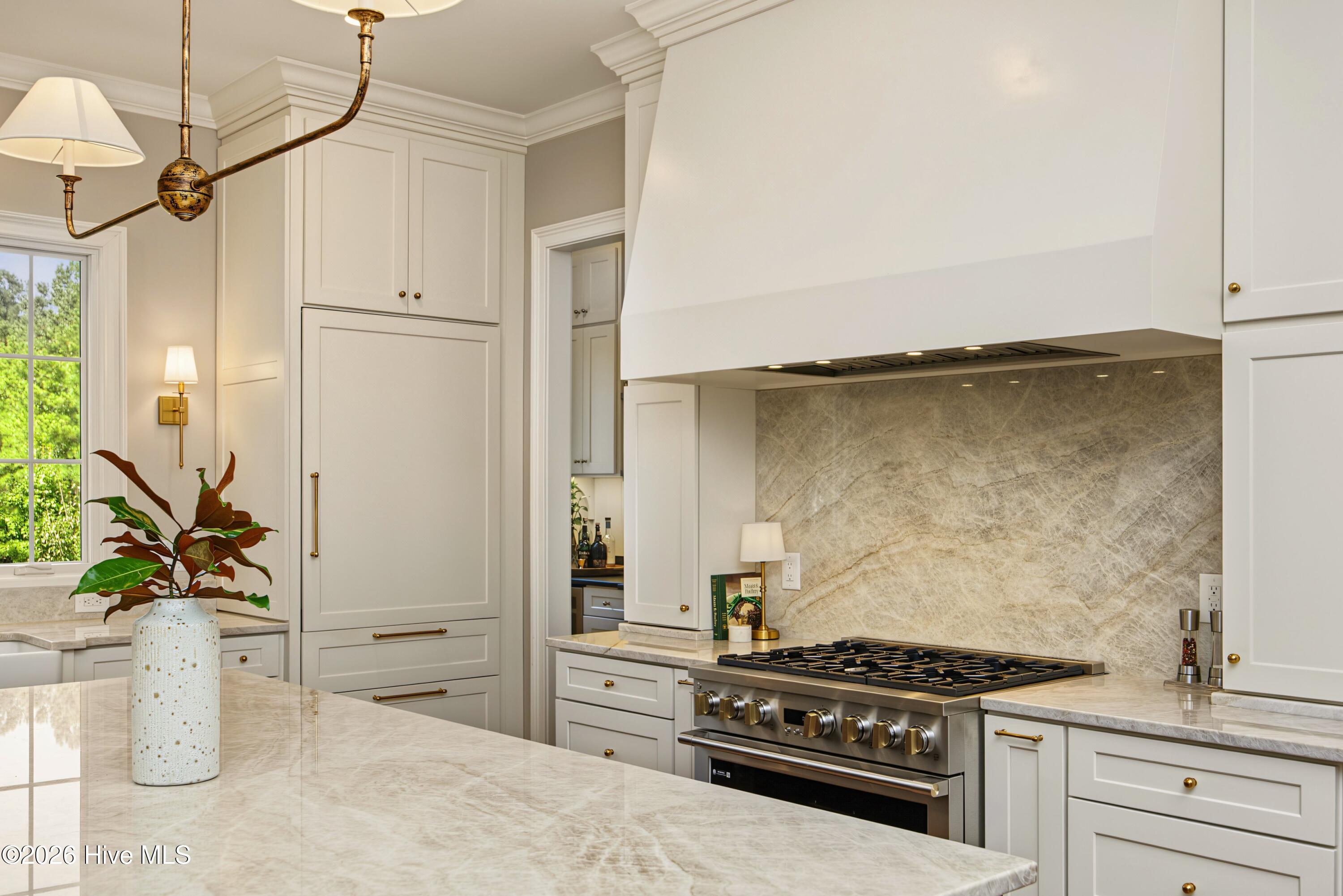 Kitchen with a marble island, white cabinetry, and a stainless steel range beneath a large hood.