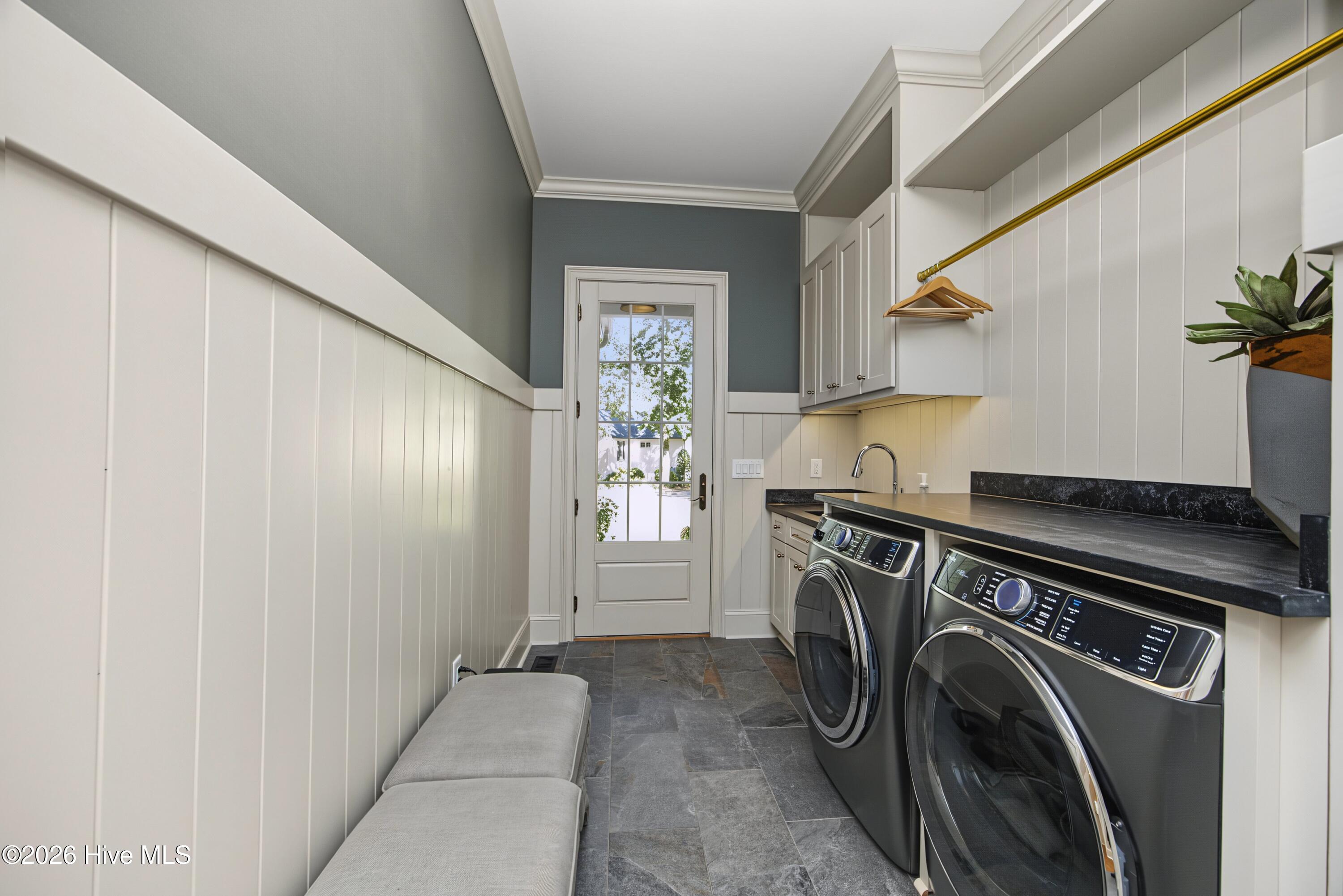 Laundry room with front-loading washer and dryer, white cabinets, dark countertop, and a glass-paneled door.