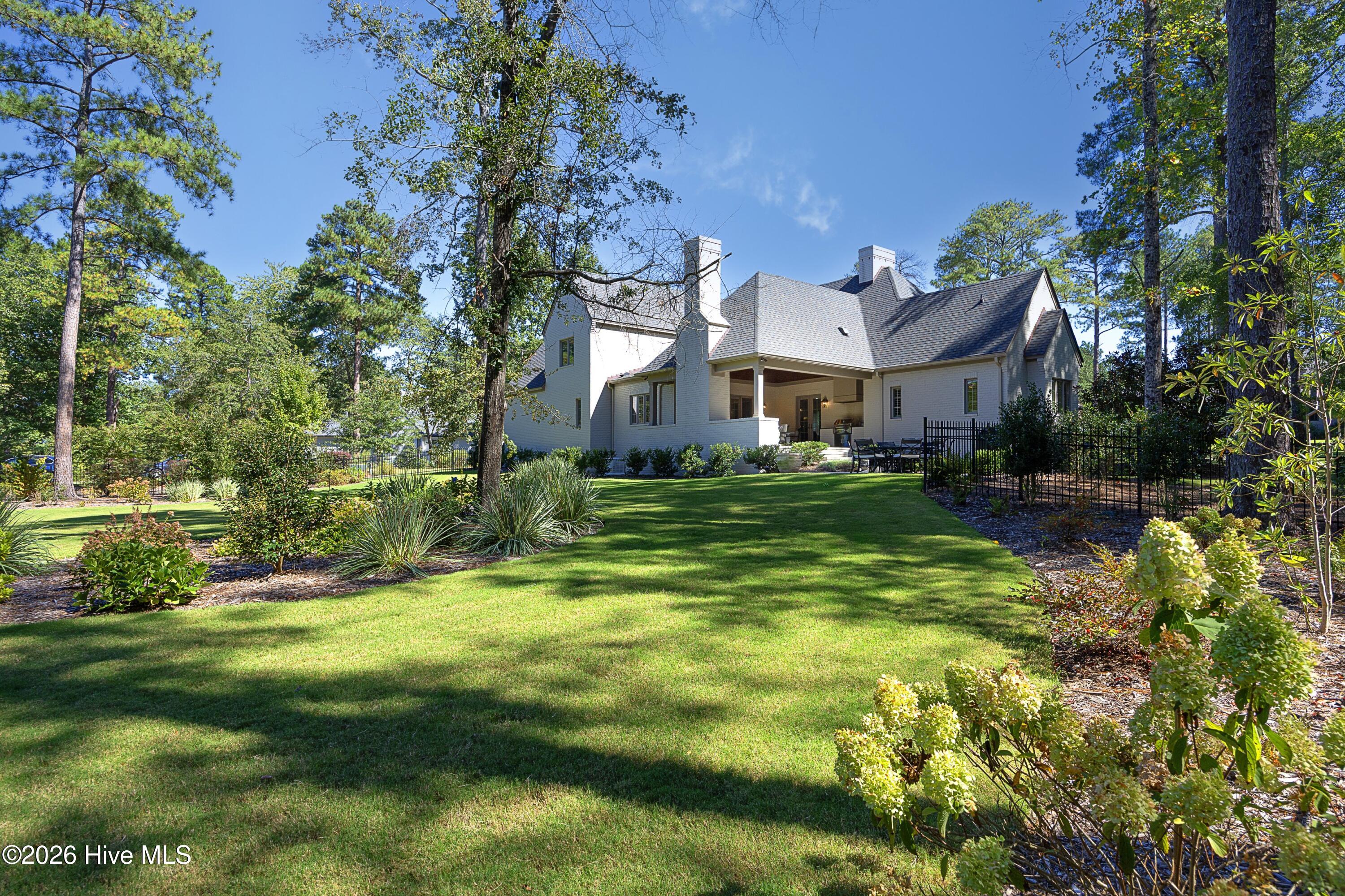 Home with a covered patio and outdoor dining area overlooking a landscaped lawn and mature trees.