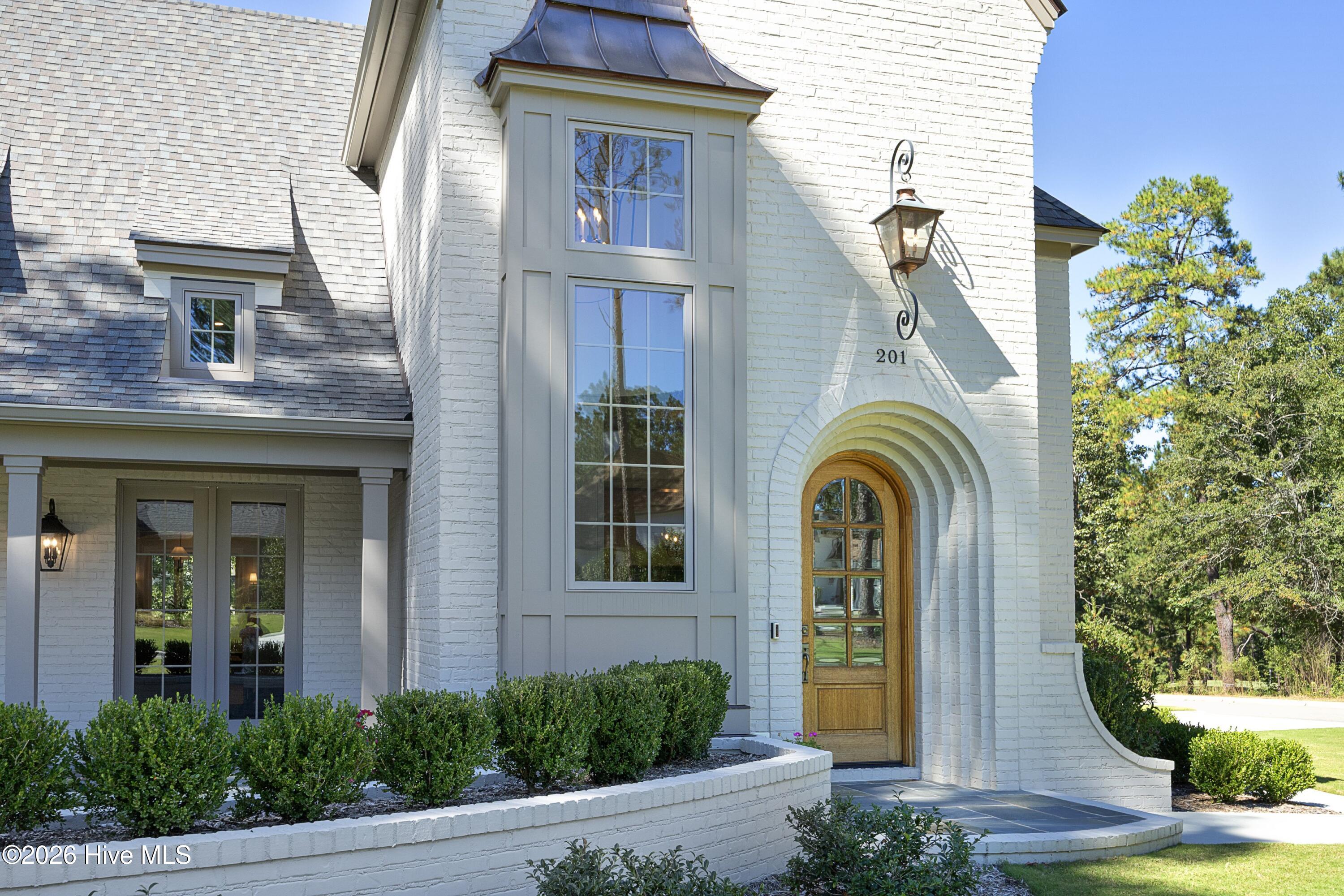 White-brick home entrance with an arched wood-and-glass door and tall windows.