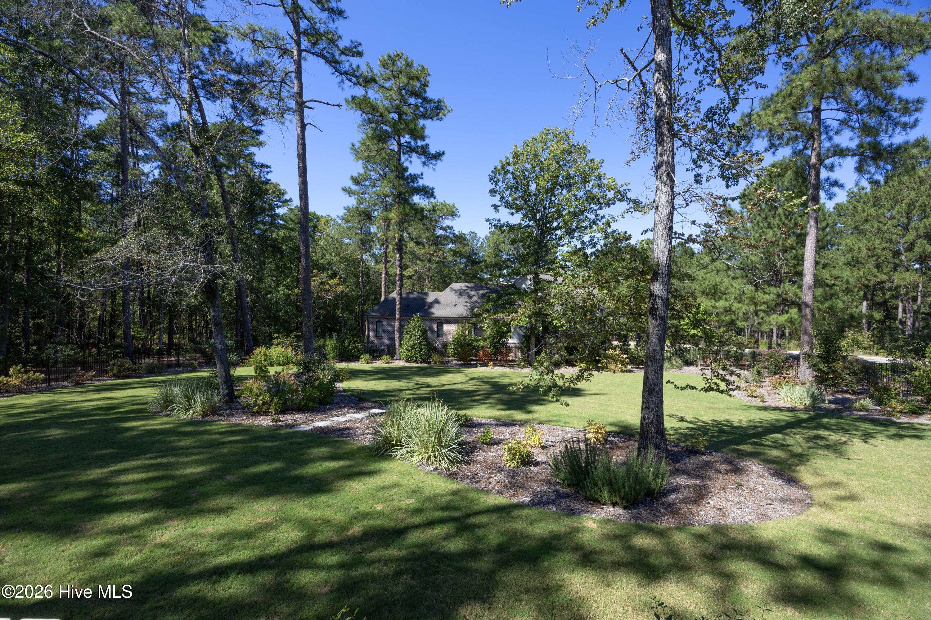 Brick house beyond a landscaped lawn, framed by mature trees and curved garden beds.
