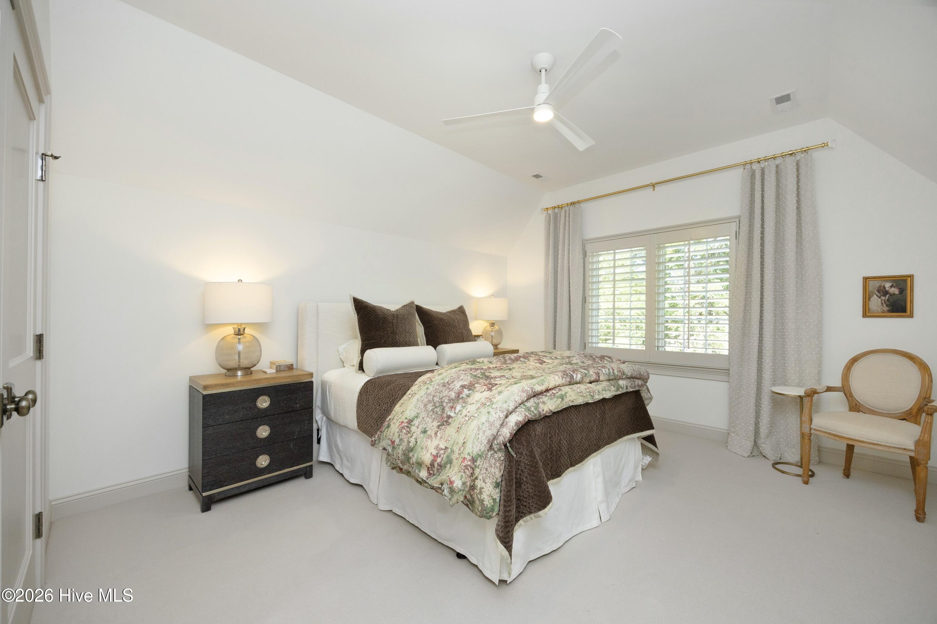 Furnished bedroom with a floral quilt, plantation-shuttered window, and white ceiling fan.