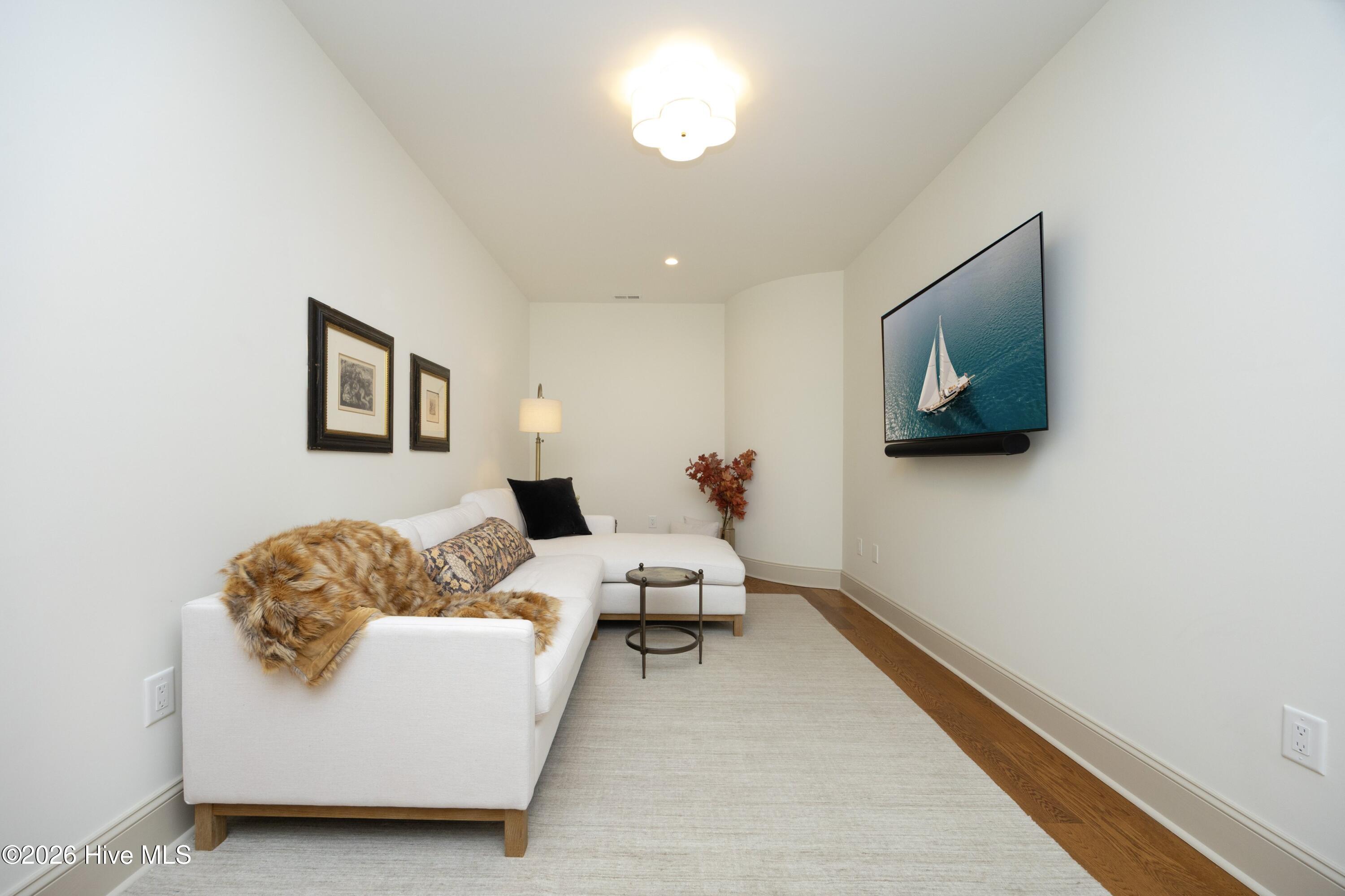Narrow living room with a white sectional sofa and wall-mounted television showing a sailboat.