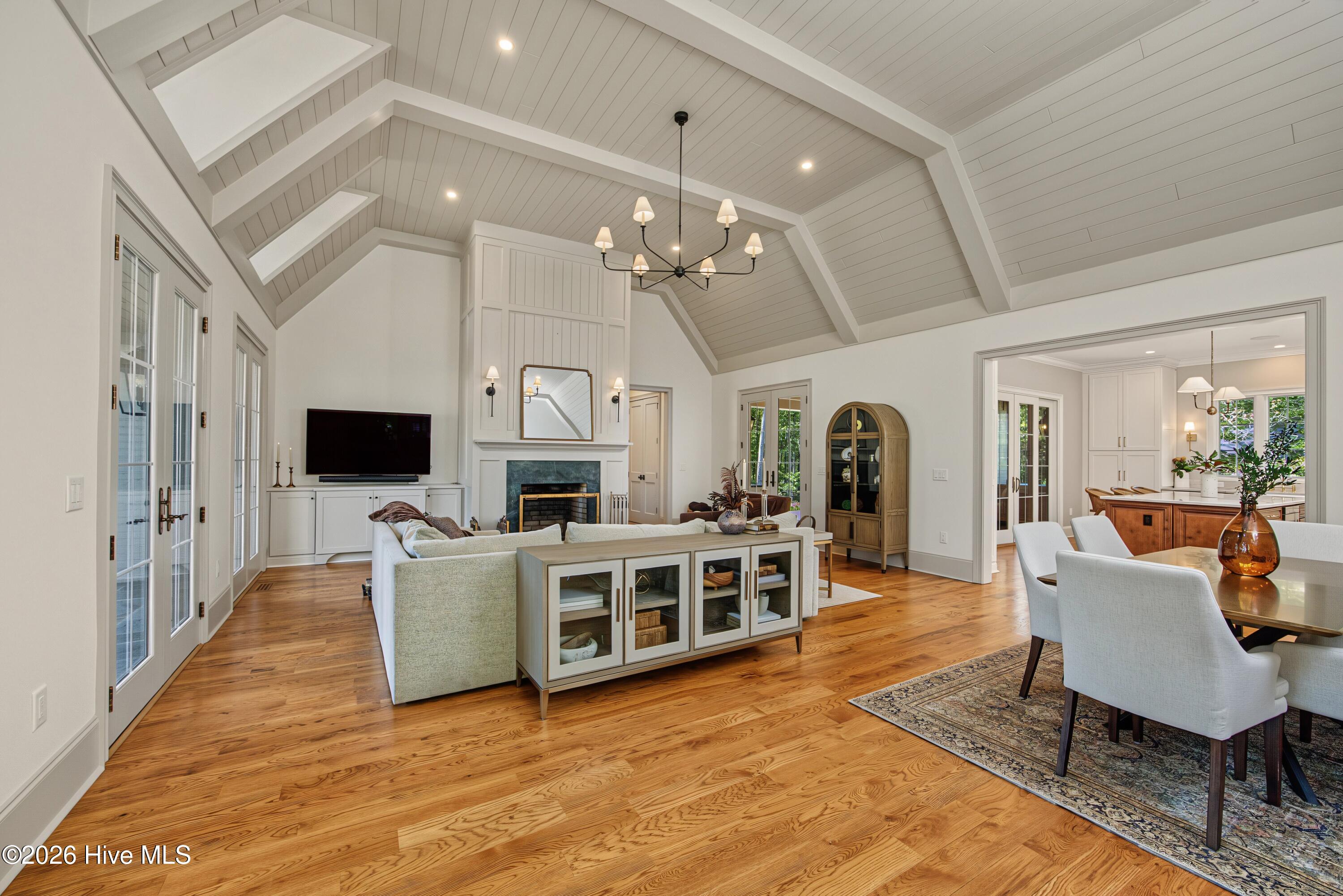 Living room with vaulted beamed ceiling, fireplace, hardwood floors, and adjoining dining area.