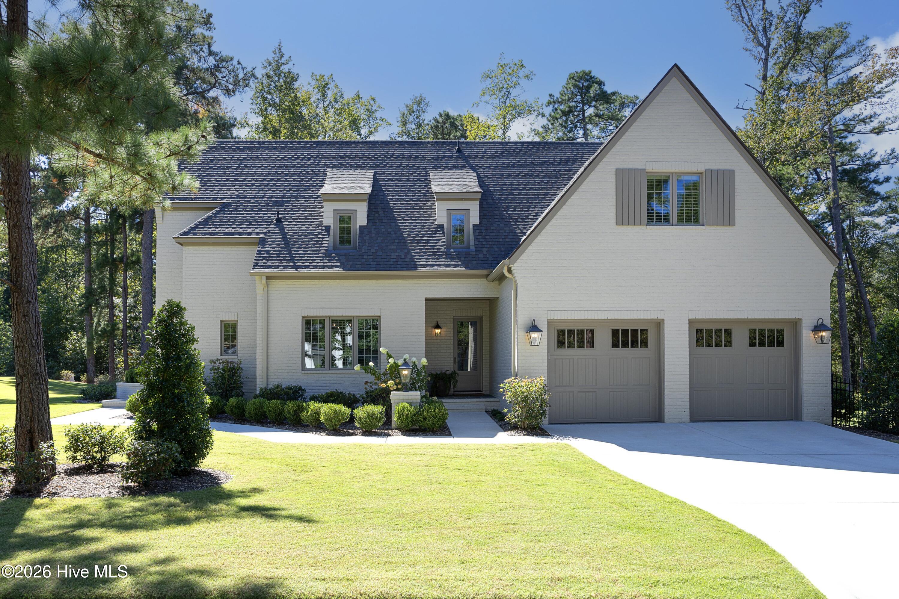 White brick home with a steep gable roof, two garage doors, and landscaped front lawn.