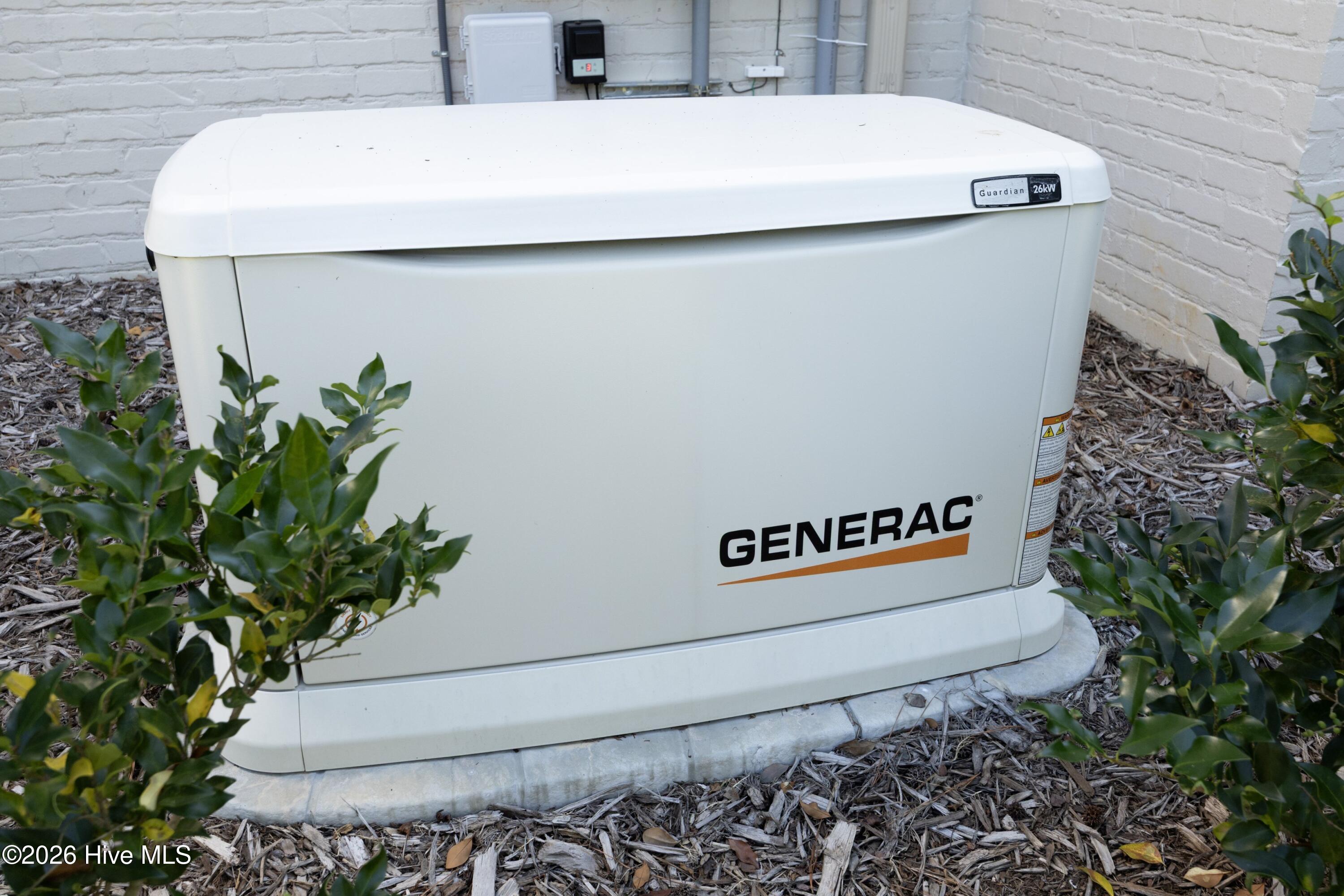 White Generac 26kW standby generator on a concrete pad beside a brick wall.