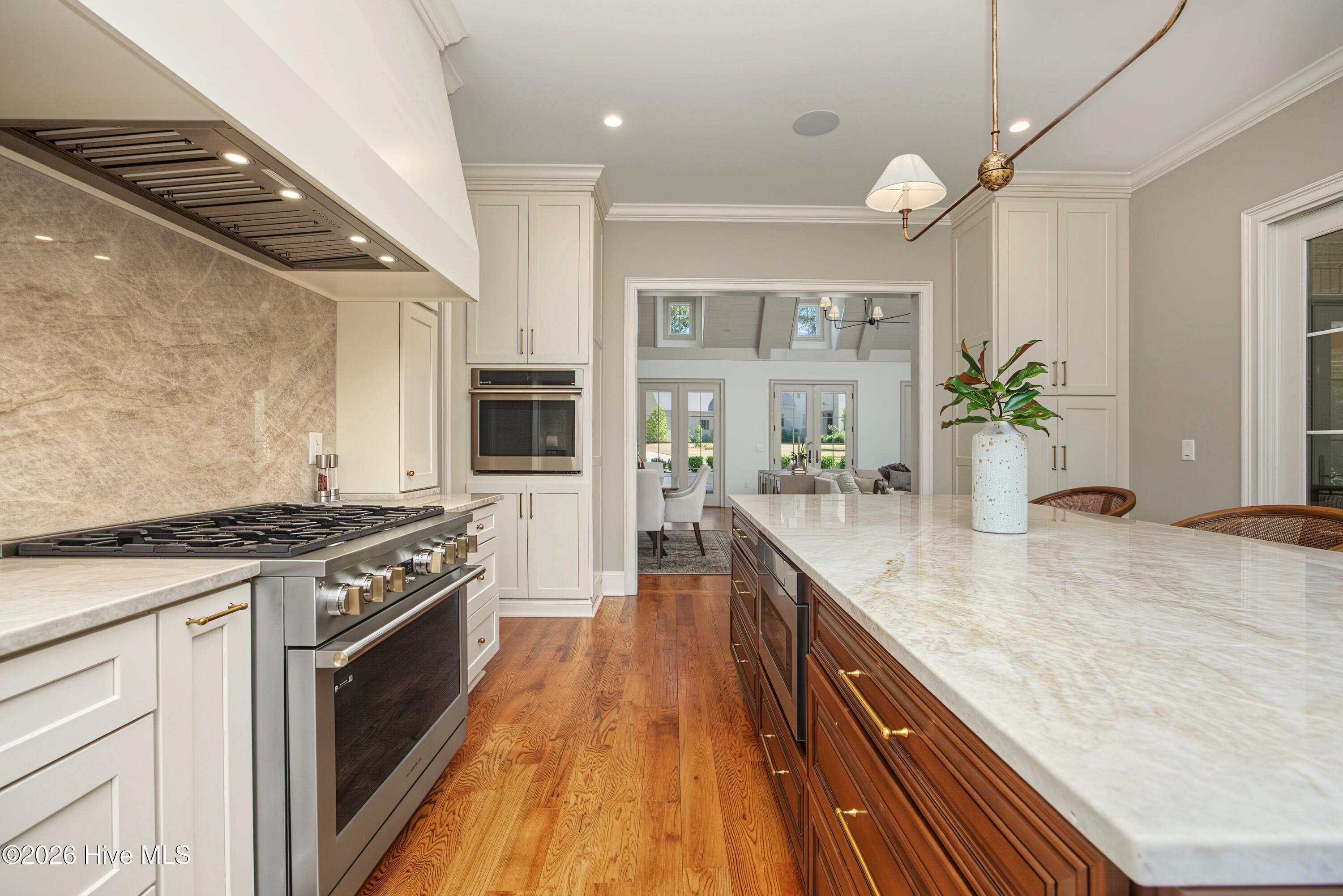 Kitchen with a large marble island, white cabinets, stainless steel range, and warm wood floors.