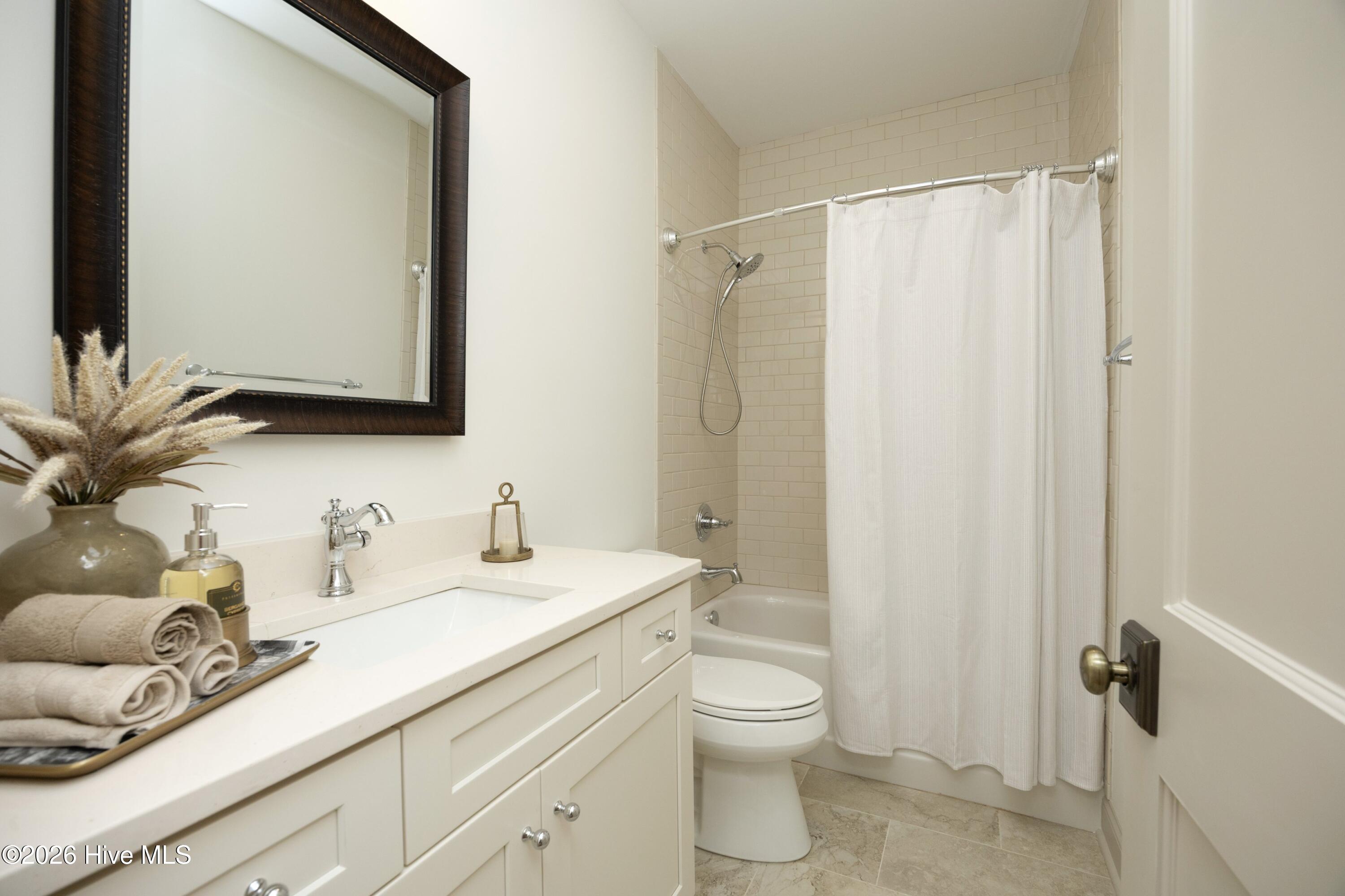 Bathroom with white vanity, dark-framed mirror, and beige tiled tub and shower.