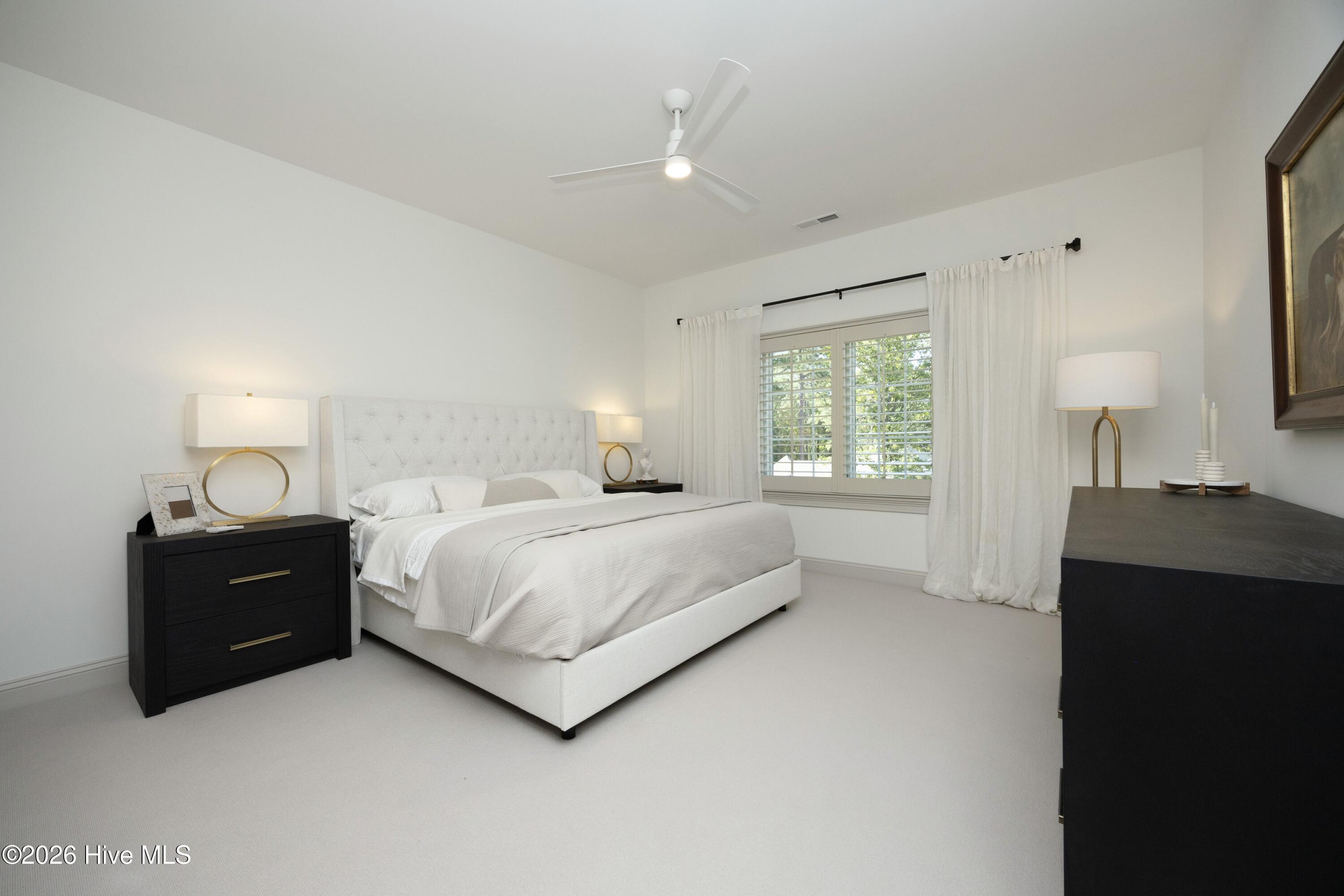 Furnished bedroom with a white tufted bed, dark nightstands, and a shuttered window.