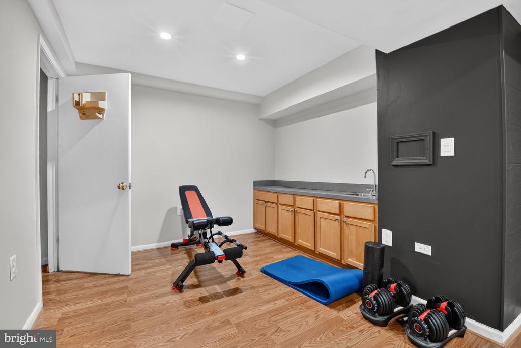 Home fitness room with a weight bench, dumbbells, blue mat, and wooden cabinets with a sink.