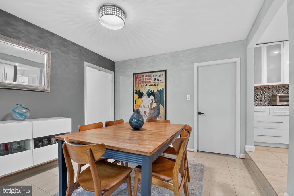 Dining room with a wooden table, gray walls, and a Moulin Rouge poster beside the kitchen.