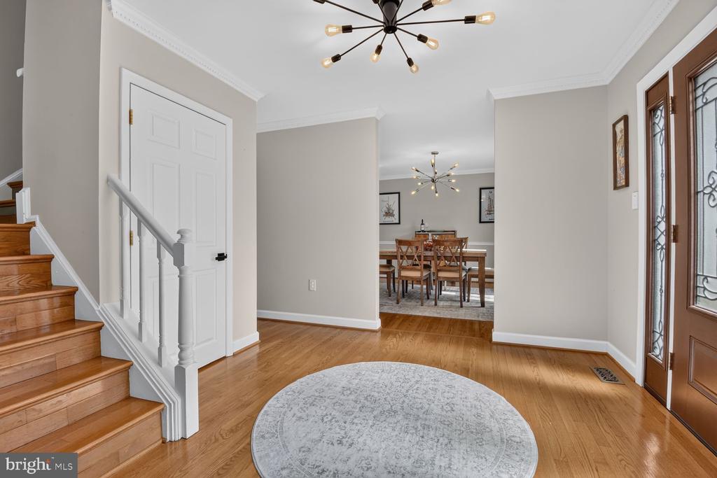 Foyer with hardwood floors, a wooden staircase, round rug, and dining room beyond.