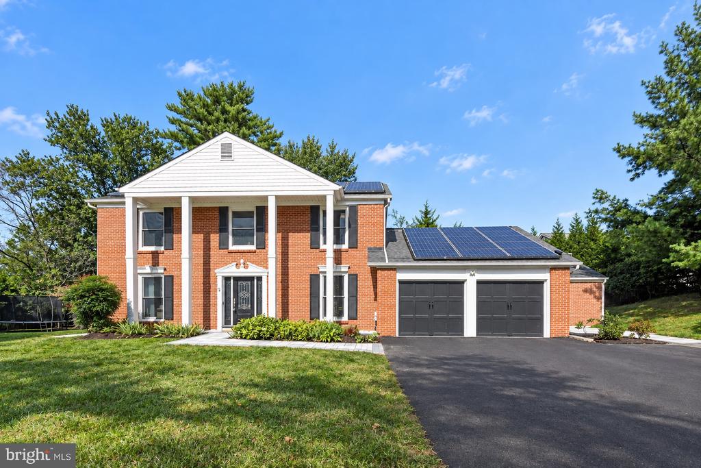 Red-brick two-story home with white columns, rooftop solar panels, and an attached two-car garage.