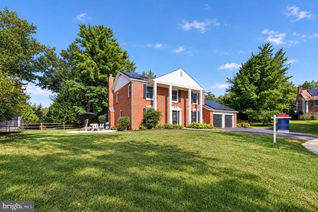 Two-story brick house with white columns, solar panels, attached garage, and a broad front lawn.
