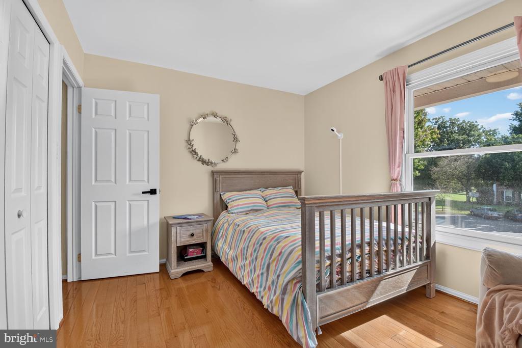 Bedroom with a wooden bed, colorful striped bedding, hardwood floors, and a large window.