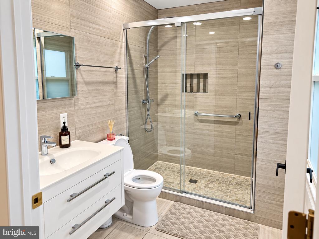 Bathroom with a glass-enclosed shower, beige tile, pebble floor, and white vanity.