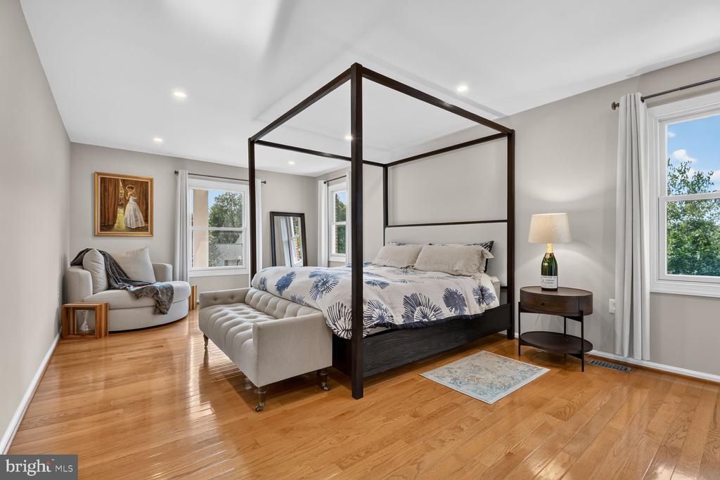 Bedroom with a dark four-poster bed, tufted bench, and sitting area by the windows.