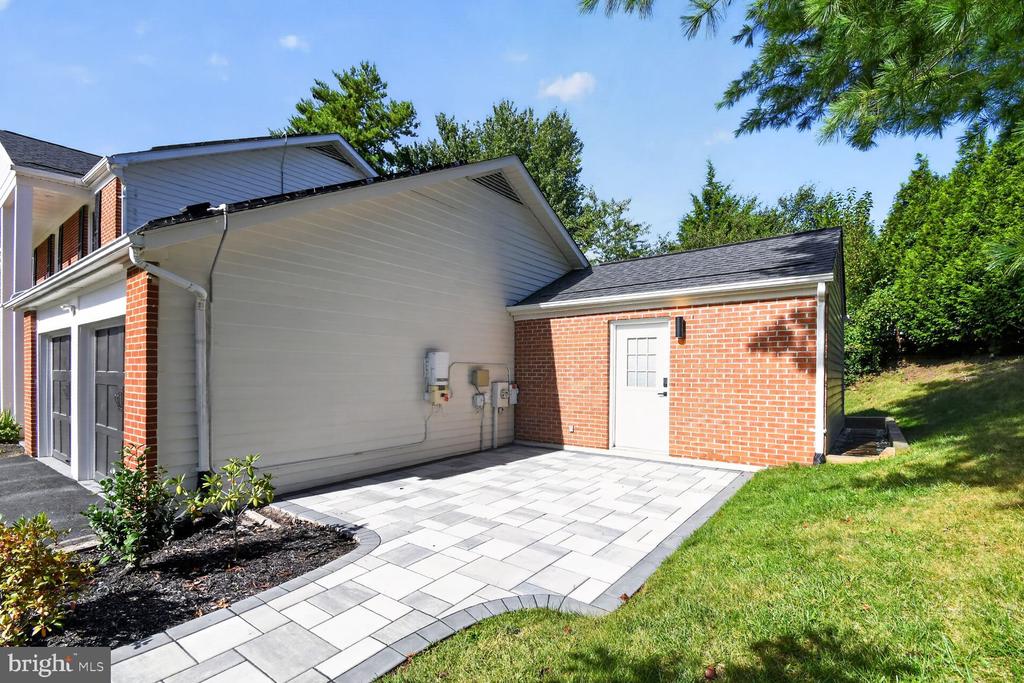 Paved patio beside a brick-and-siding home, bordered by lawn and landscaping.