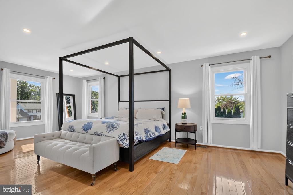 Bedroom with a black canopy bed, floral bedding, and a tufted bench on hardwood floors.